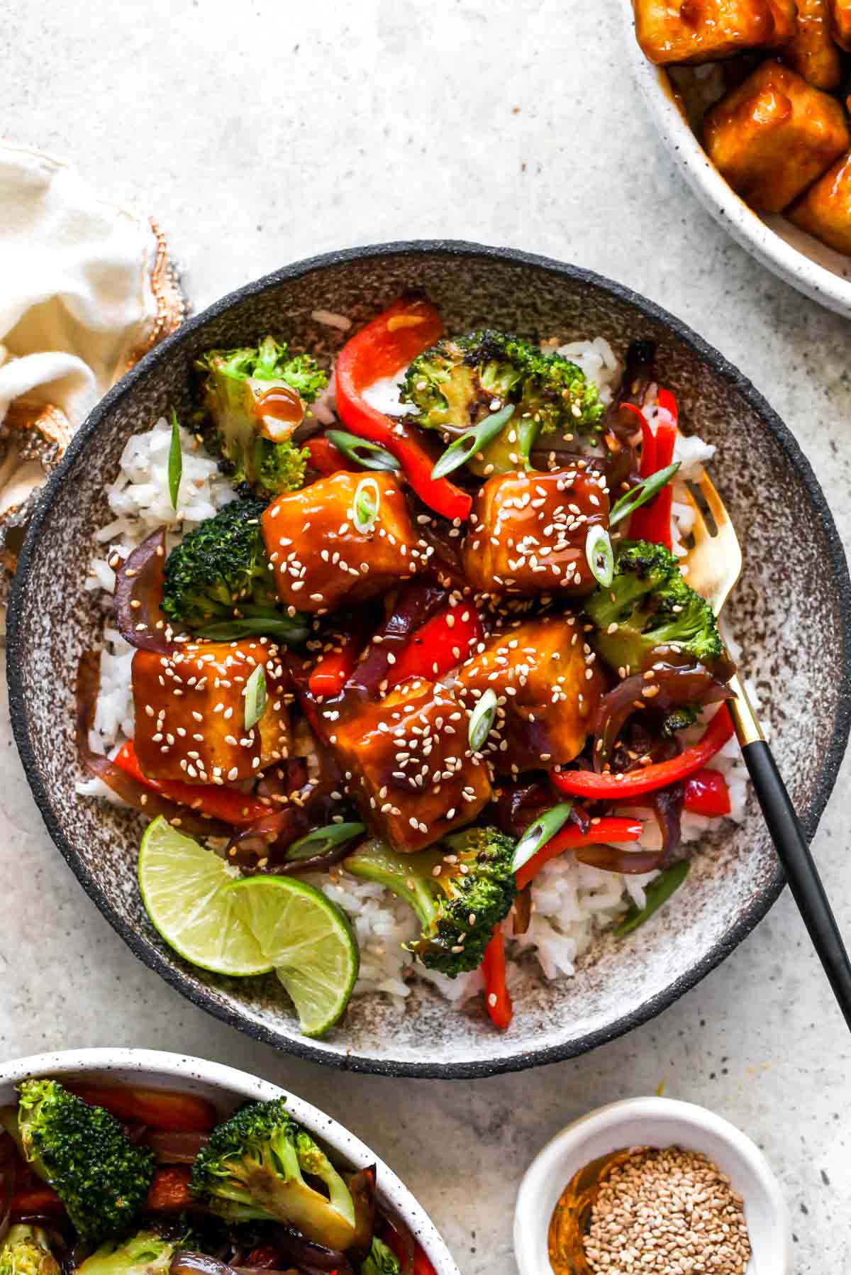 Orange tofu over rice with vegetables in a silver bowl