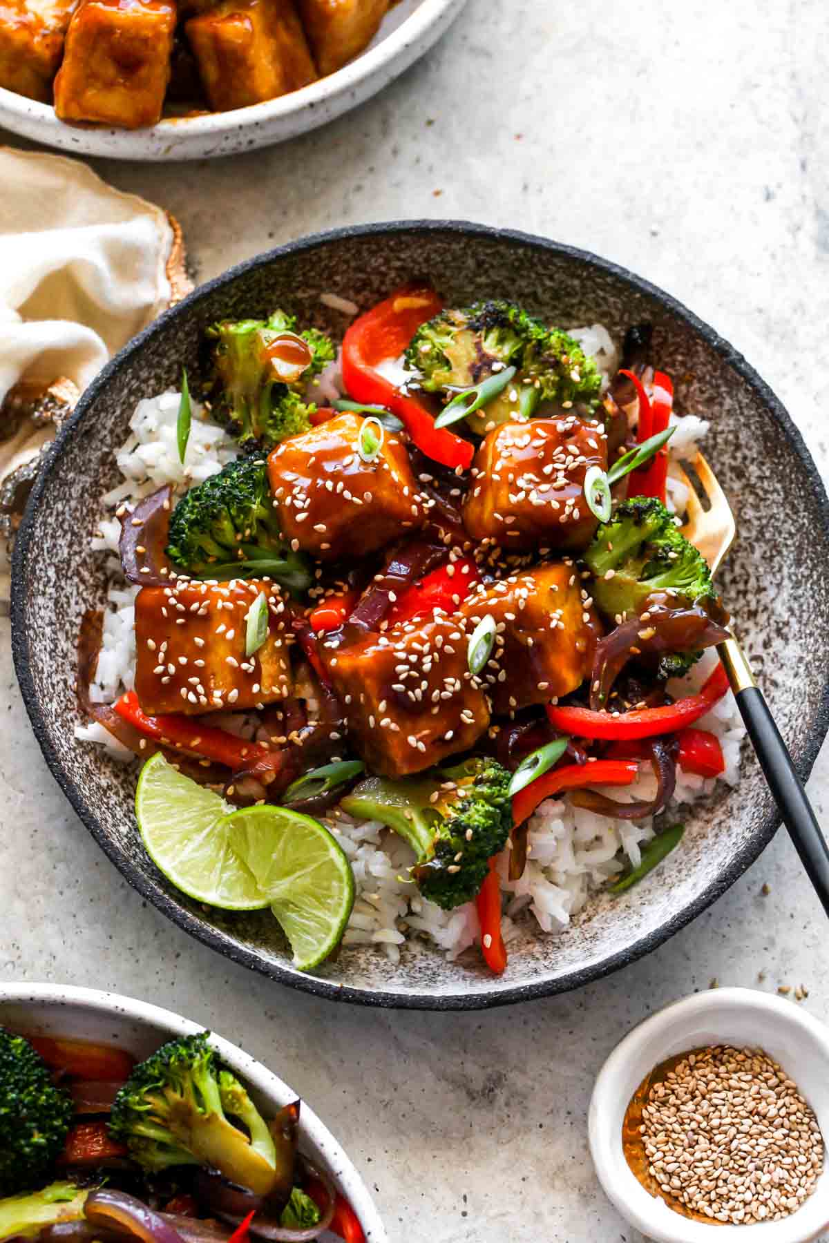 Orange tofu topped with sesame seeds and green onion in a gray bowl