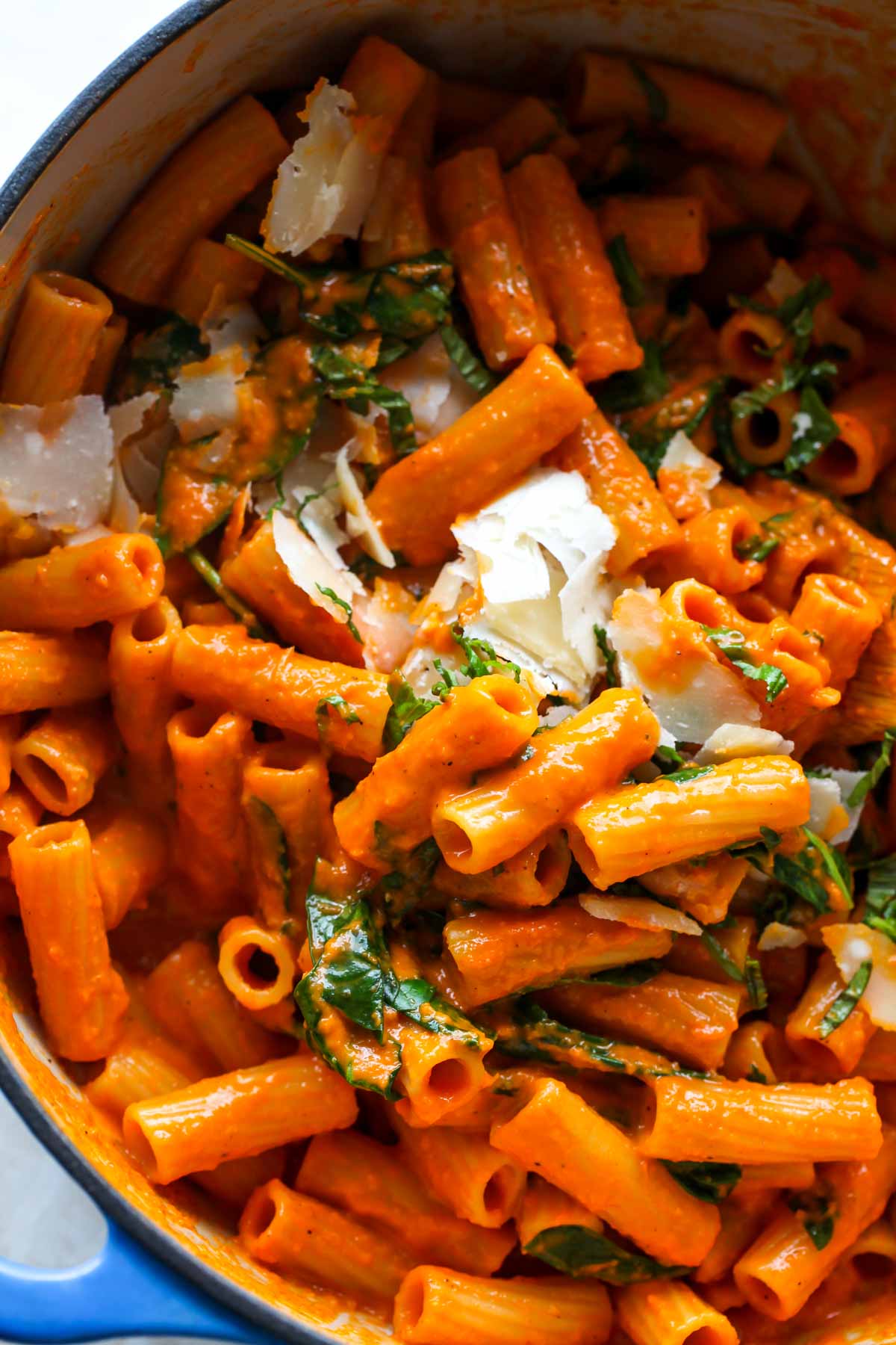 Parmesan and basil being stirred into a pot of pasta