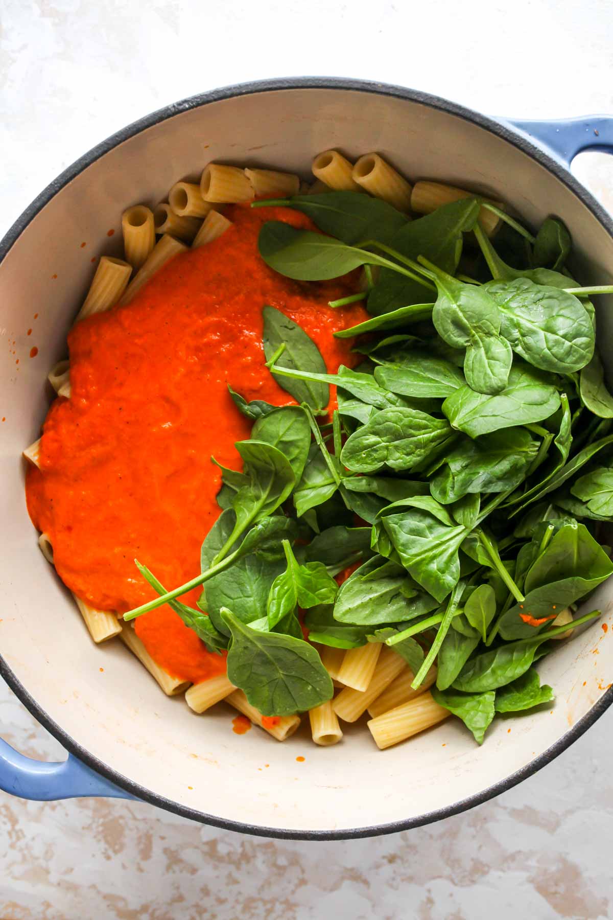 Rigatoni, spinach, and red pepper sauce being mixed in a large pot