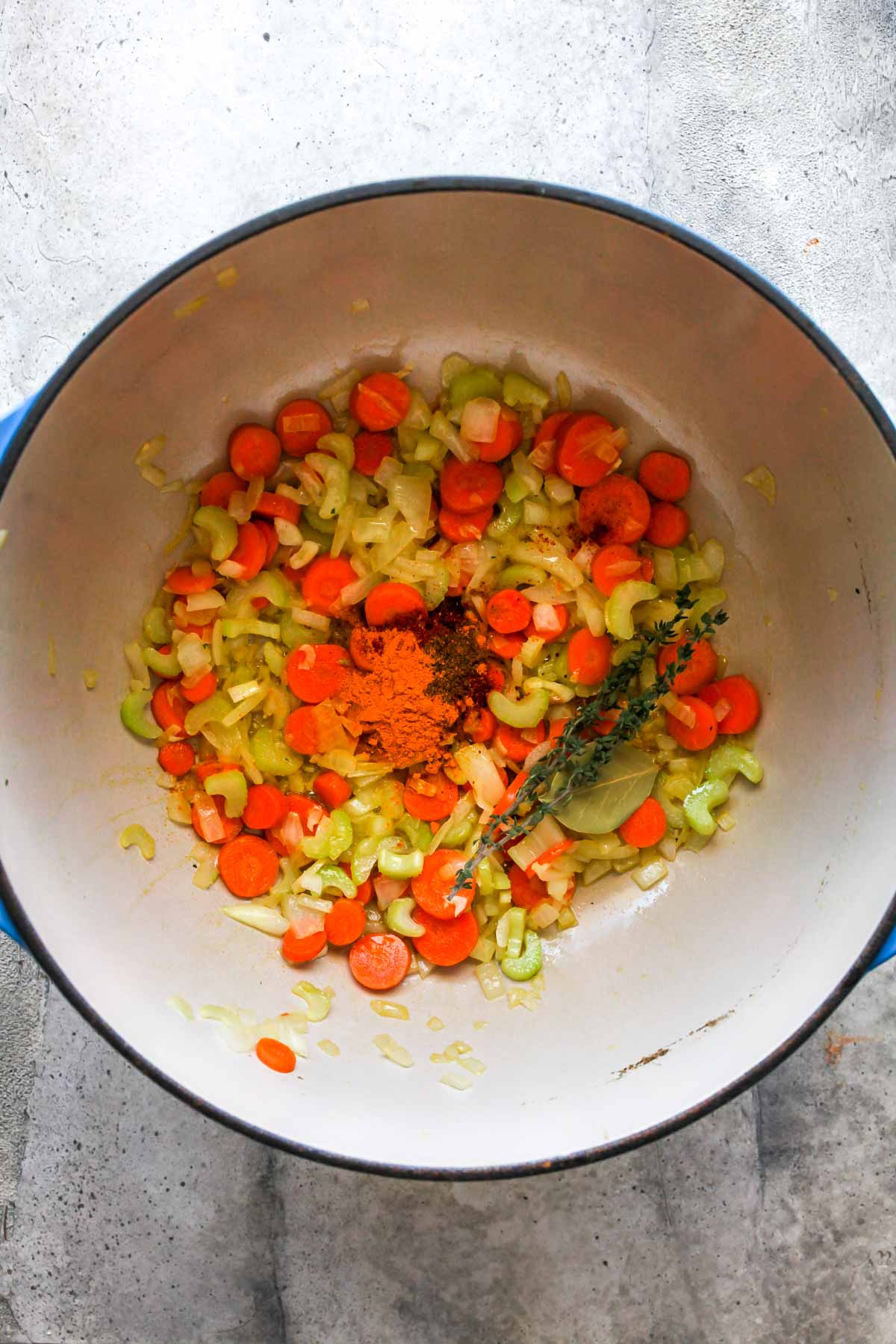 Spices, thyme, and bay leaf being added to a pot of sautéed vegetables