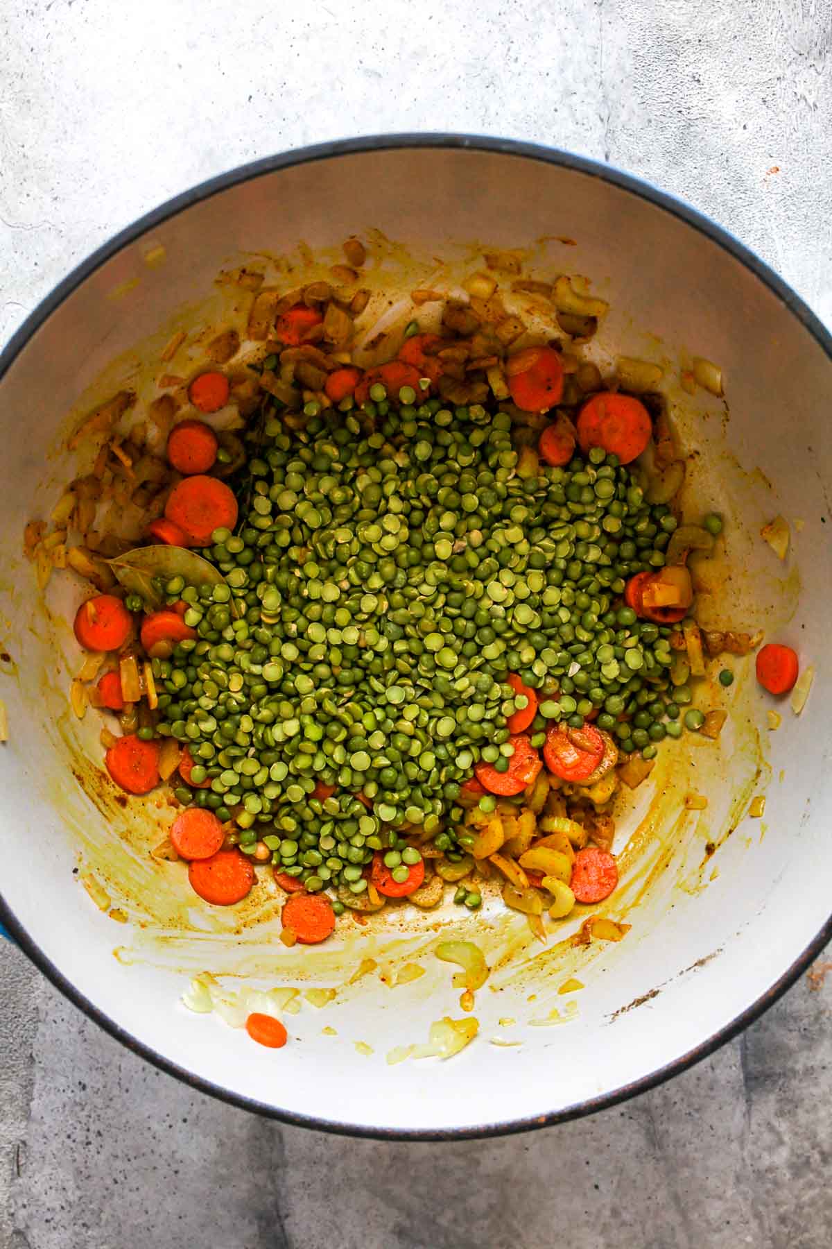 Dry split peas being mixed in a pot with sautéed veggies