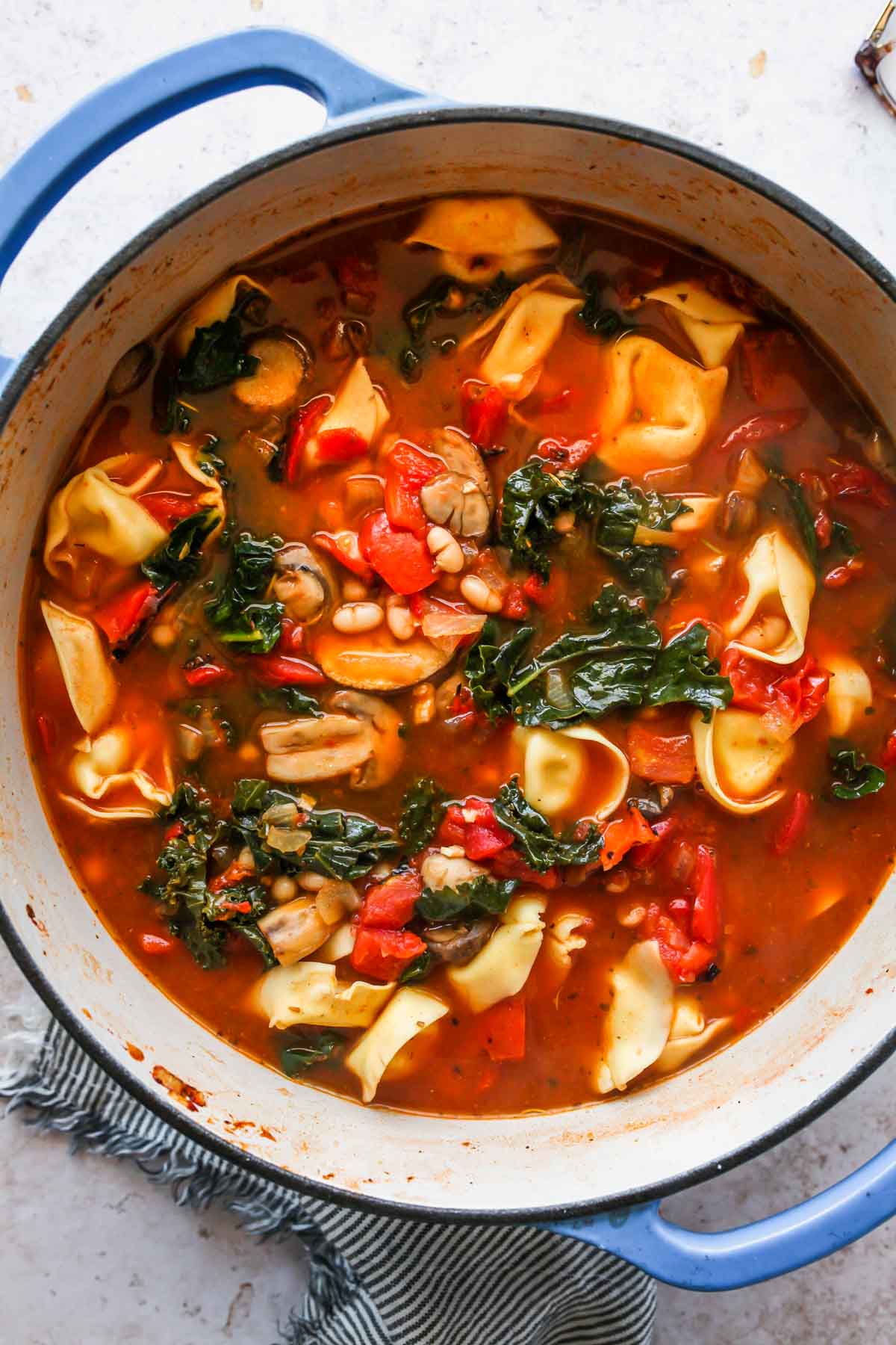 Tortellini tomato soup in a Dutch oven with kale and basil leaves