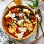 Tuscan tortellini and tomato soup in a gold bowl with basil garnish