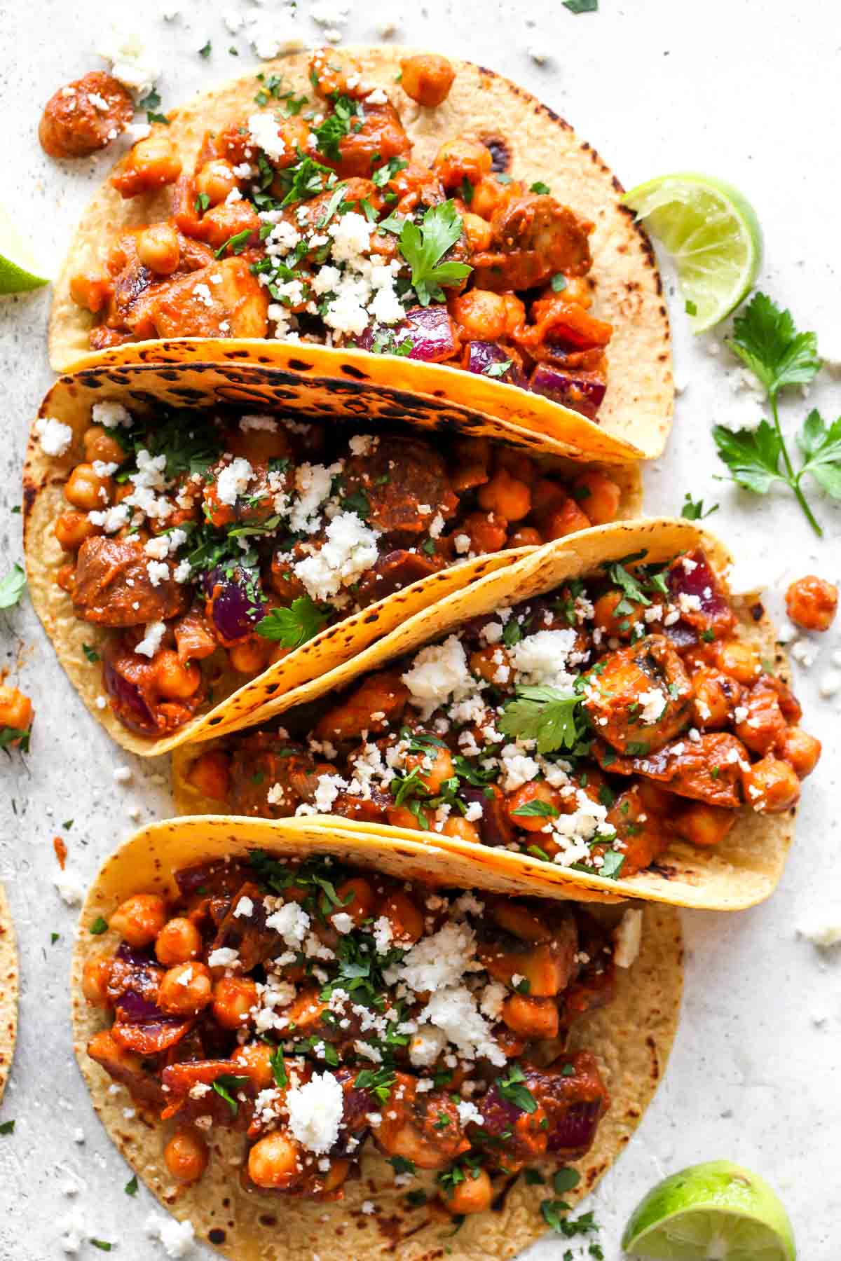 Four vegan tacos on a gray platter topped with cilantro, cheese, and onion