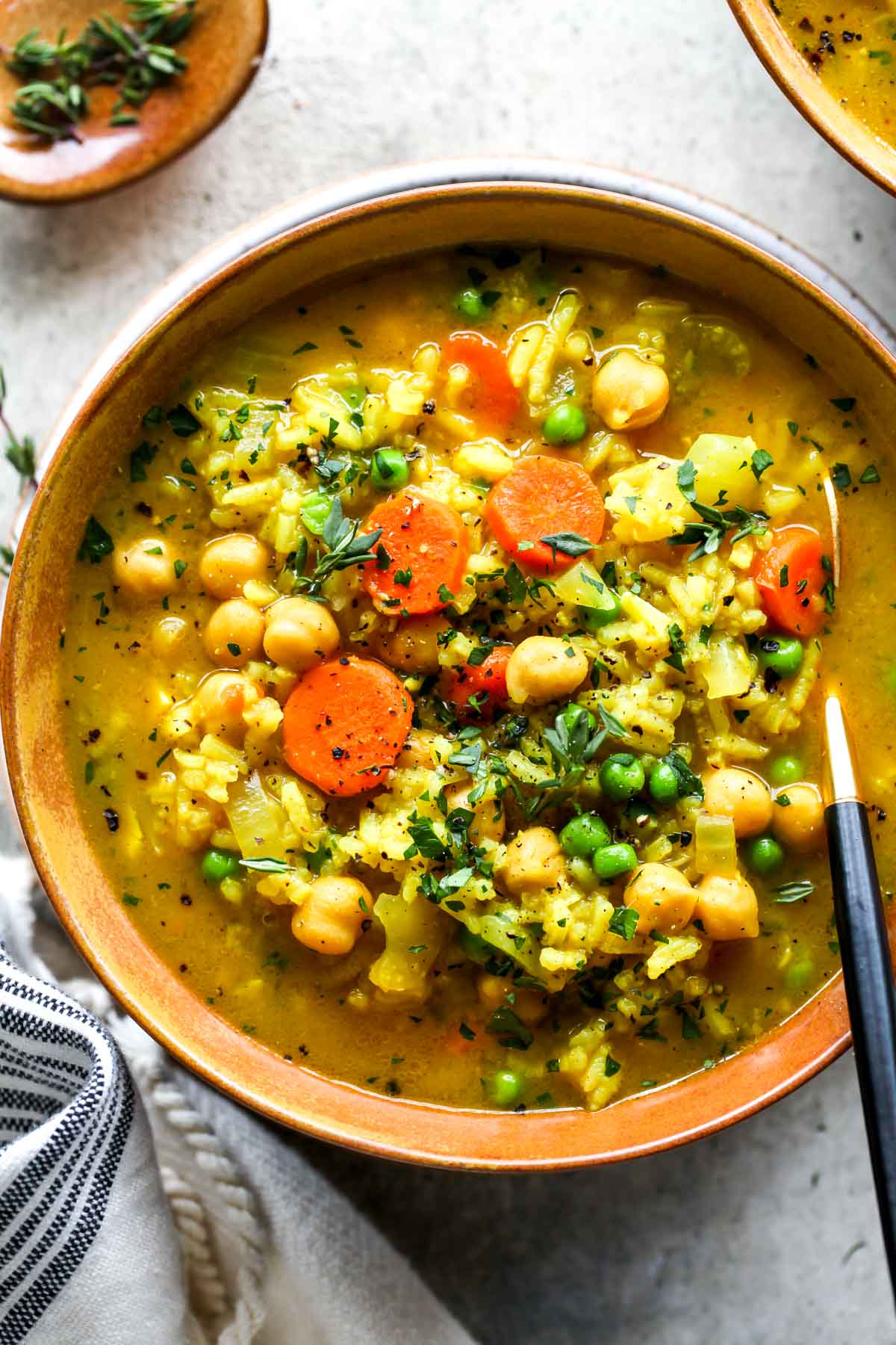 Chickpea and rice soup in a gold bowl topped with fresh thyme