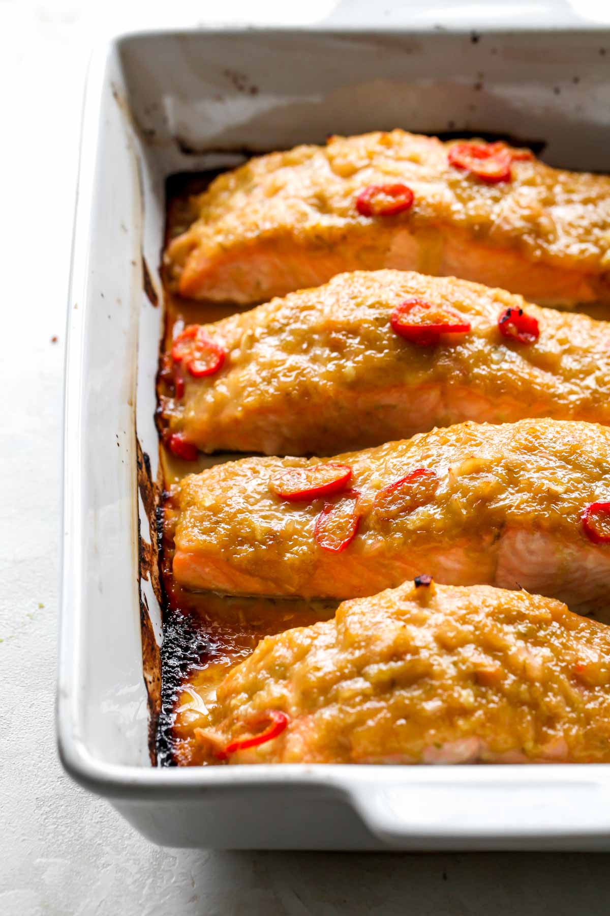 Four salmon fillets coated in a marinade in a roasting pan