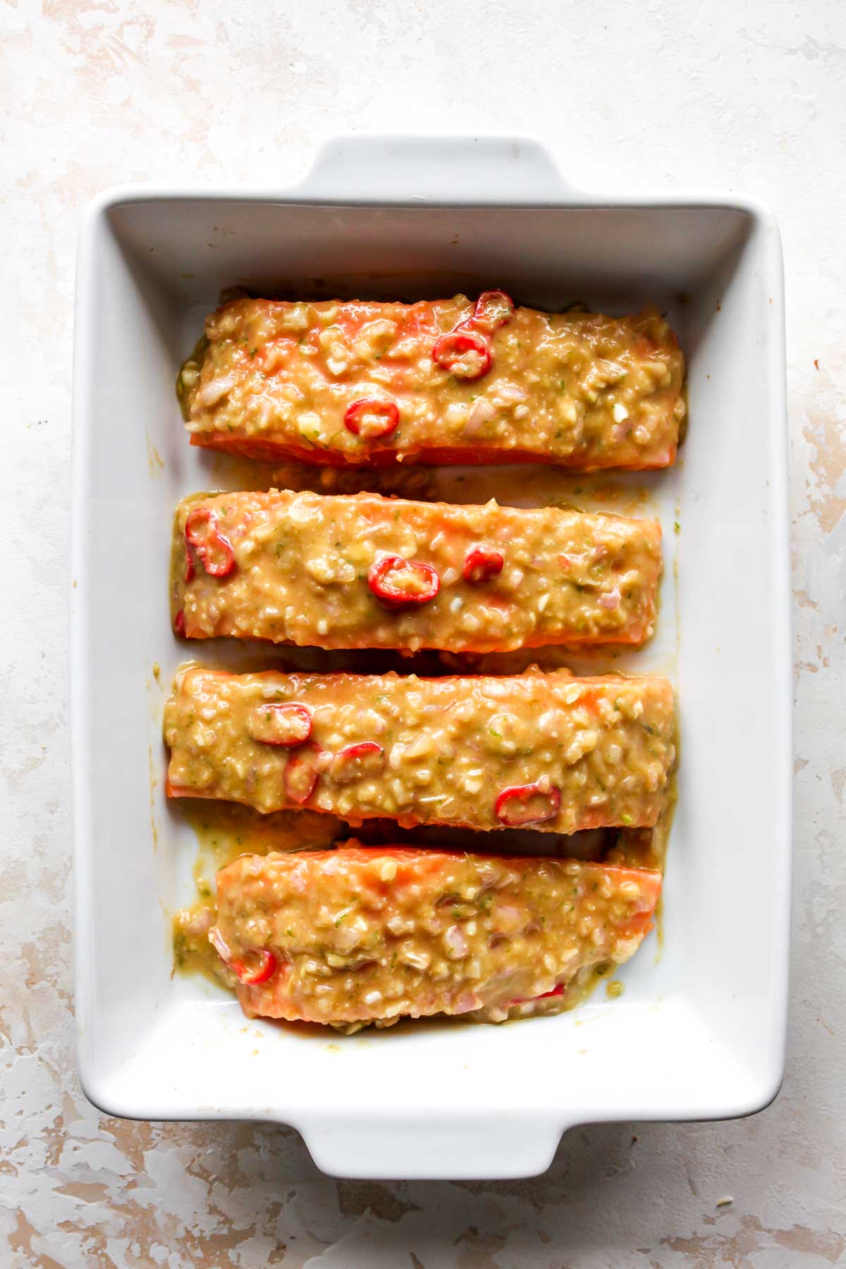 Salmon fillets in a baking dish being coated in marinade