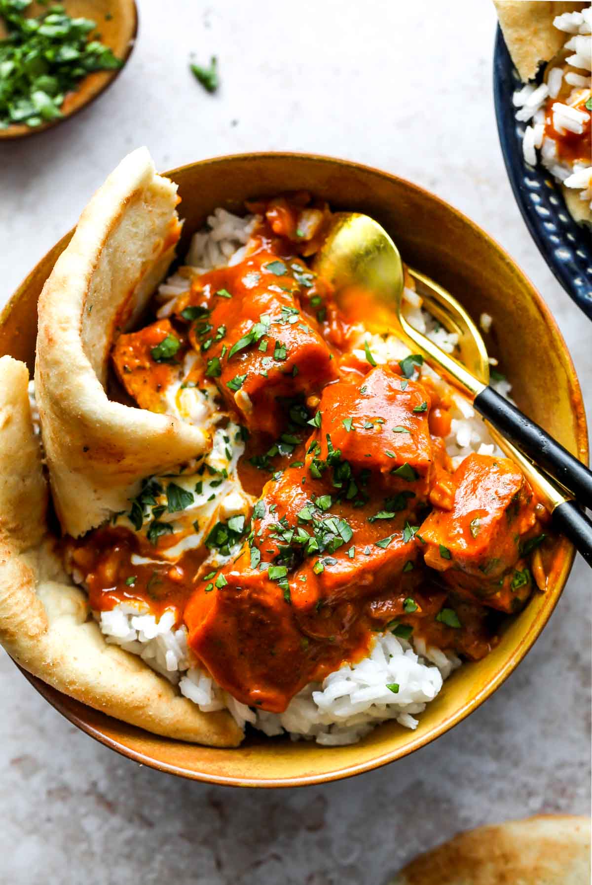 Gold bowl filled with rice, tofu, masala sauce, and naan bread