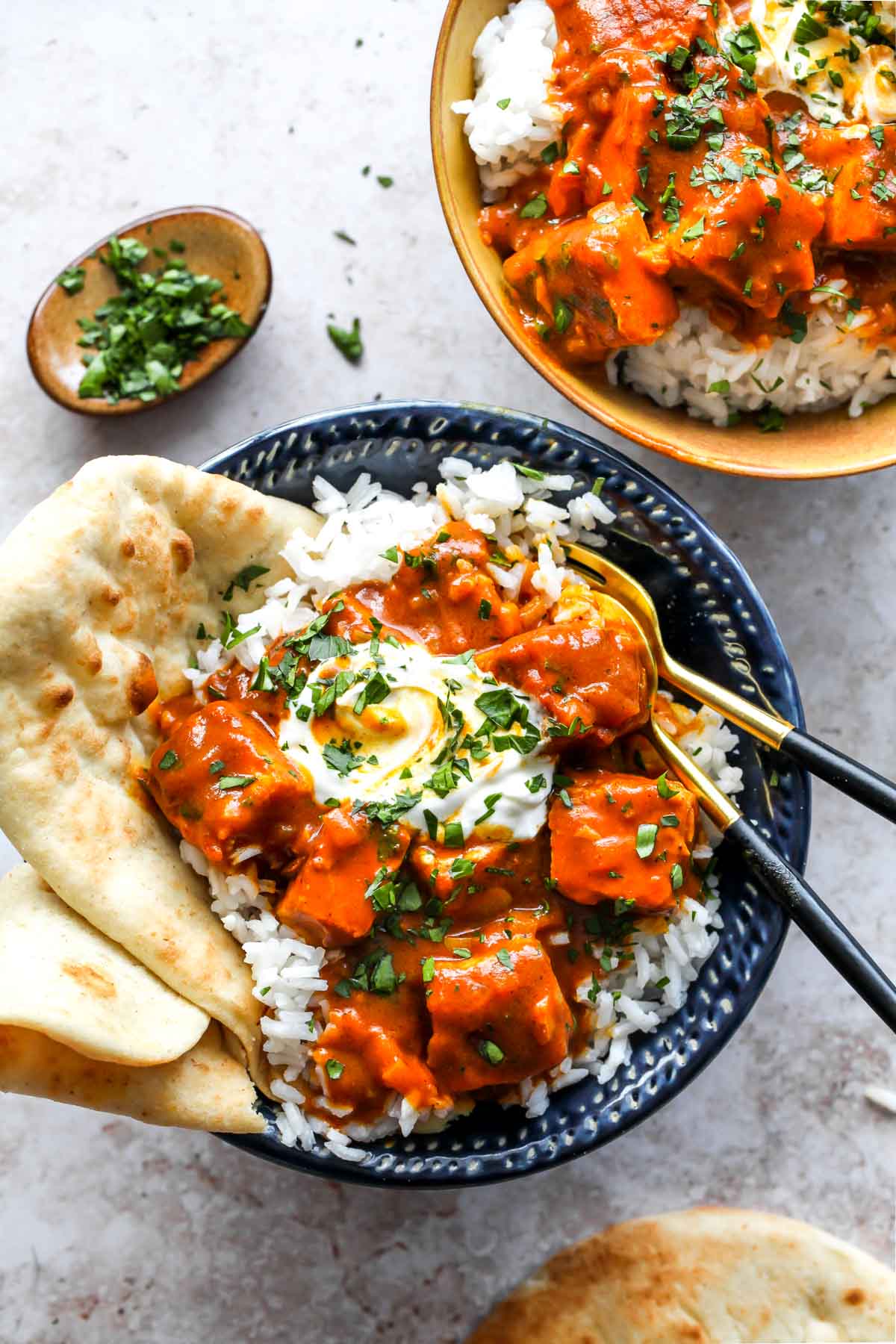 Two bowls of vegan tikka masala topped with yogurt, herbs, and naan bread