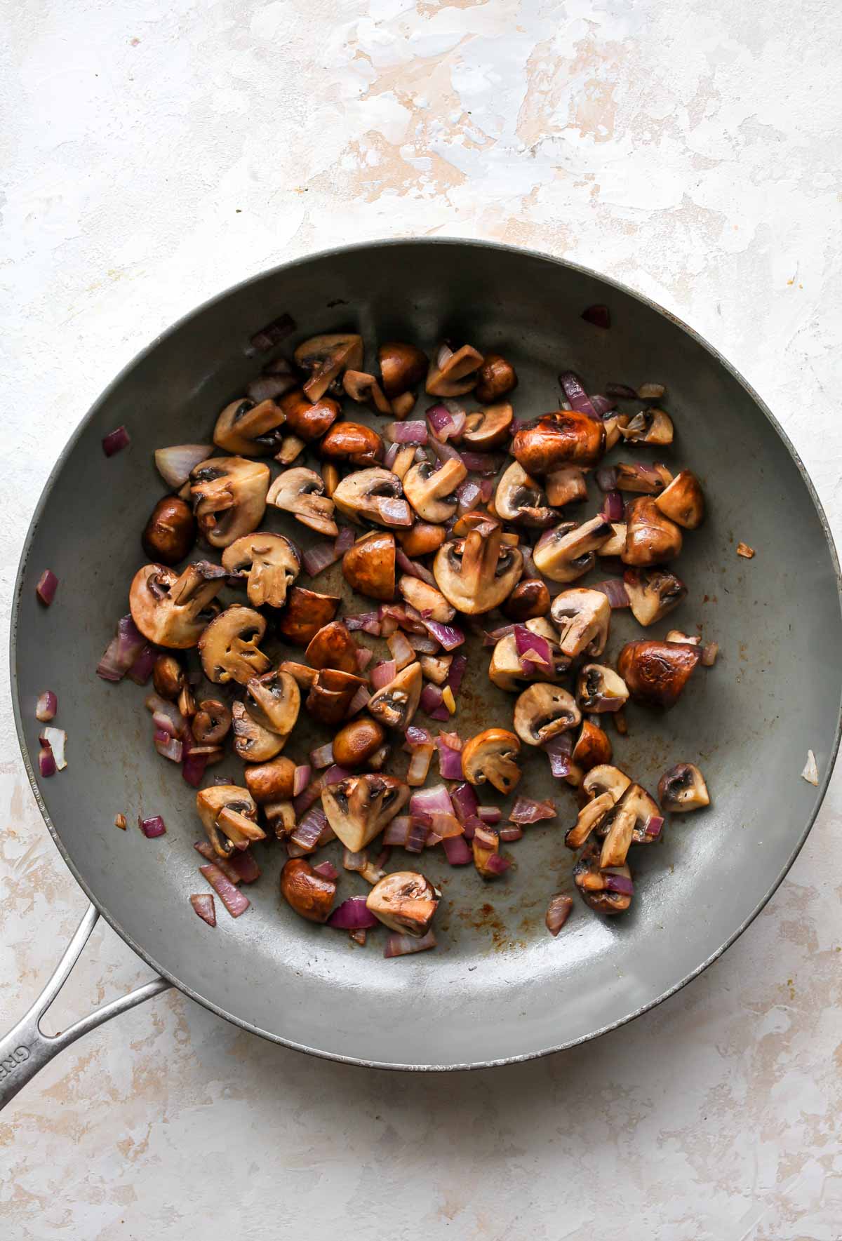 Mushrooms and red onion being sauteed in a skillet