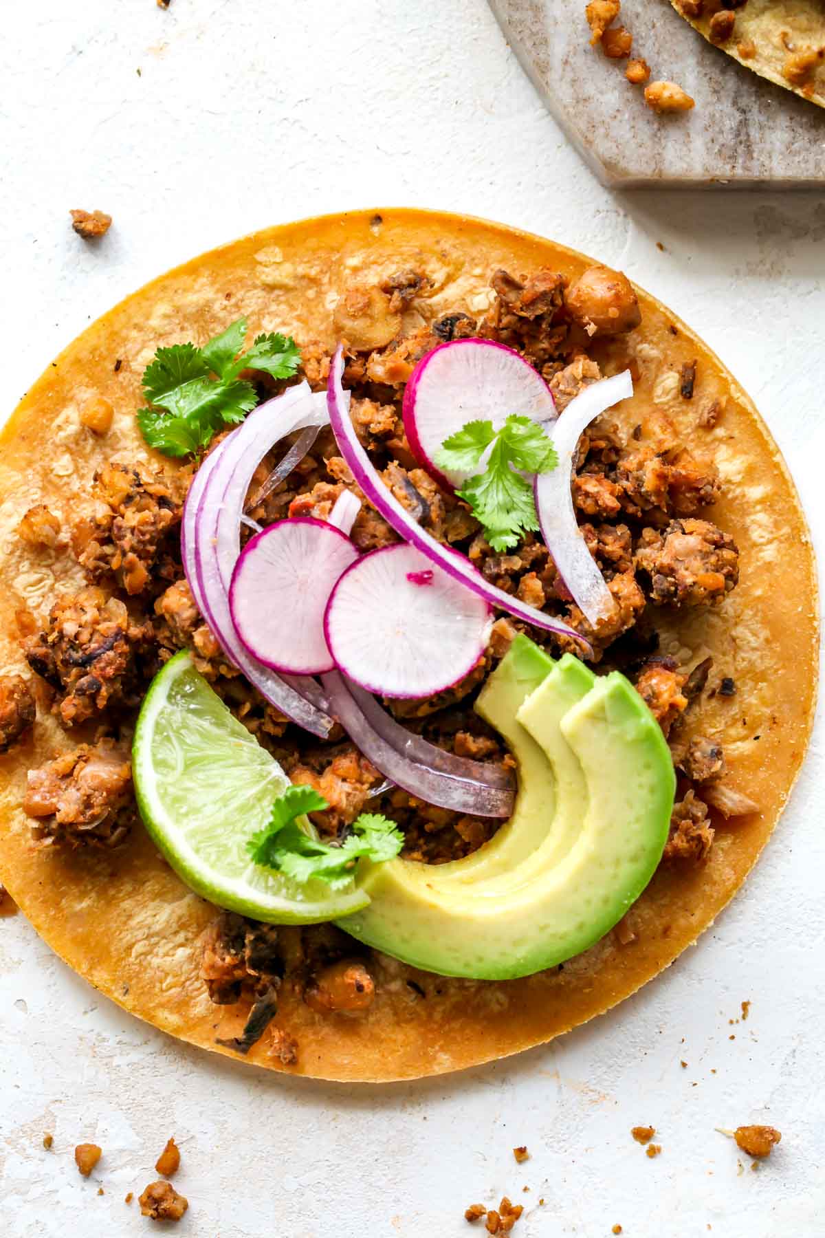 One vegan chorizo taco on a white surface topped with avocado, red onion, and radish slices