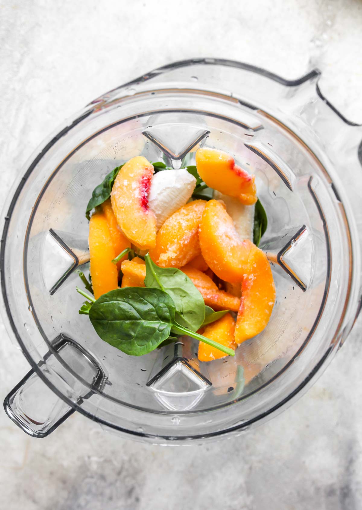 Frozen peaches, spinach, banana, and milk in a blender