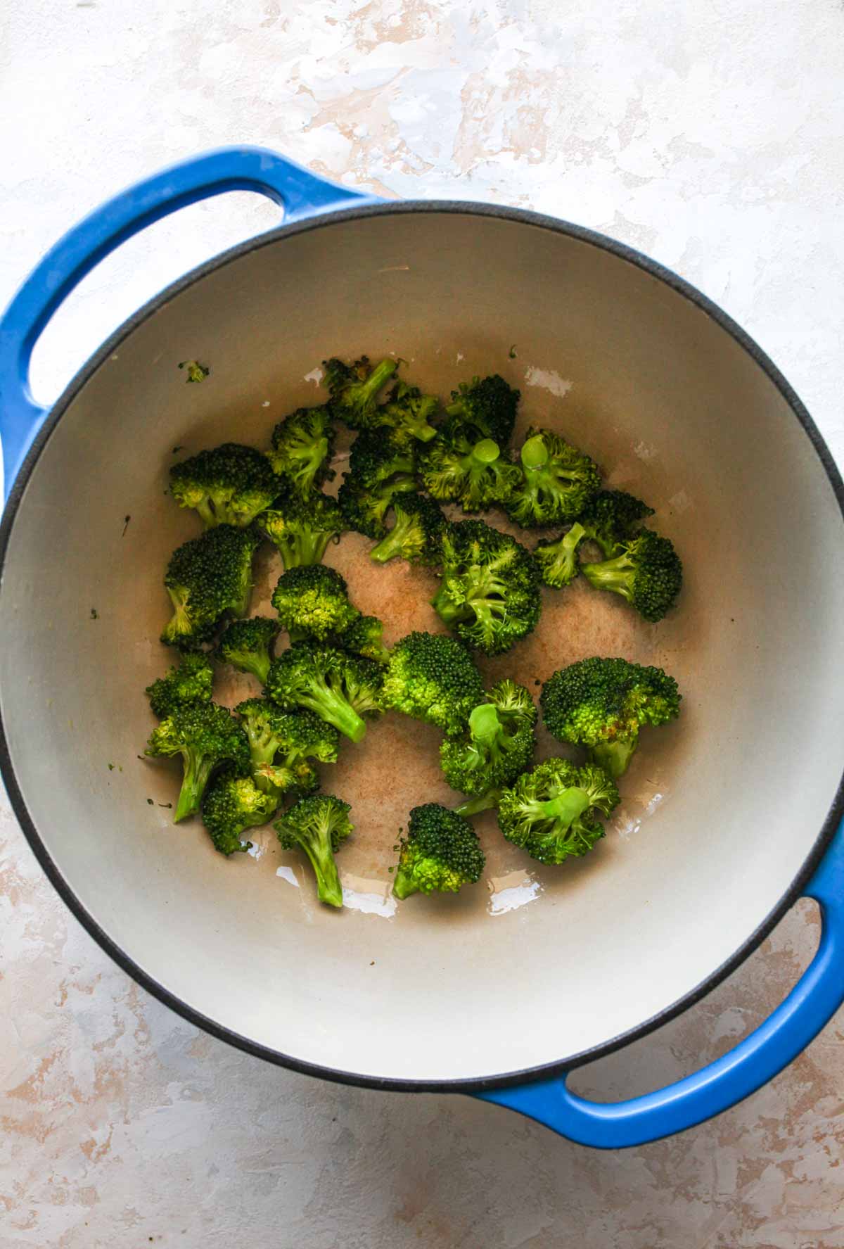 Broccoli florets being cooked in a blue Dutch oven