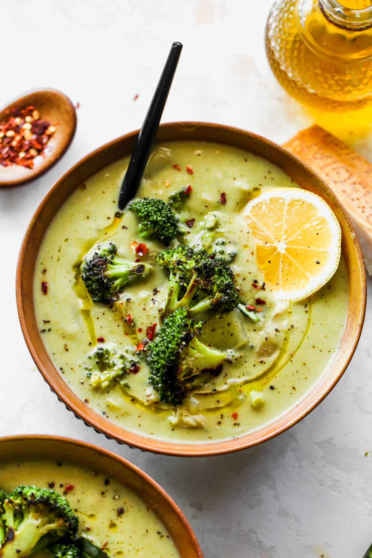 Two bowls of creamy broccoli soup topped with broccoli florets and chili flakes
