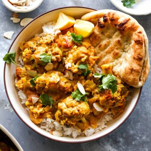 Cauliflower curry over rice in a tan bowl with naan bread on the side