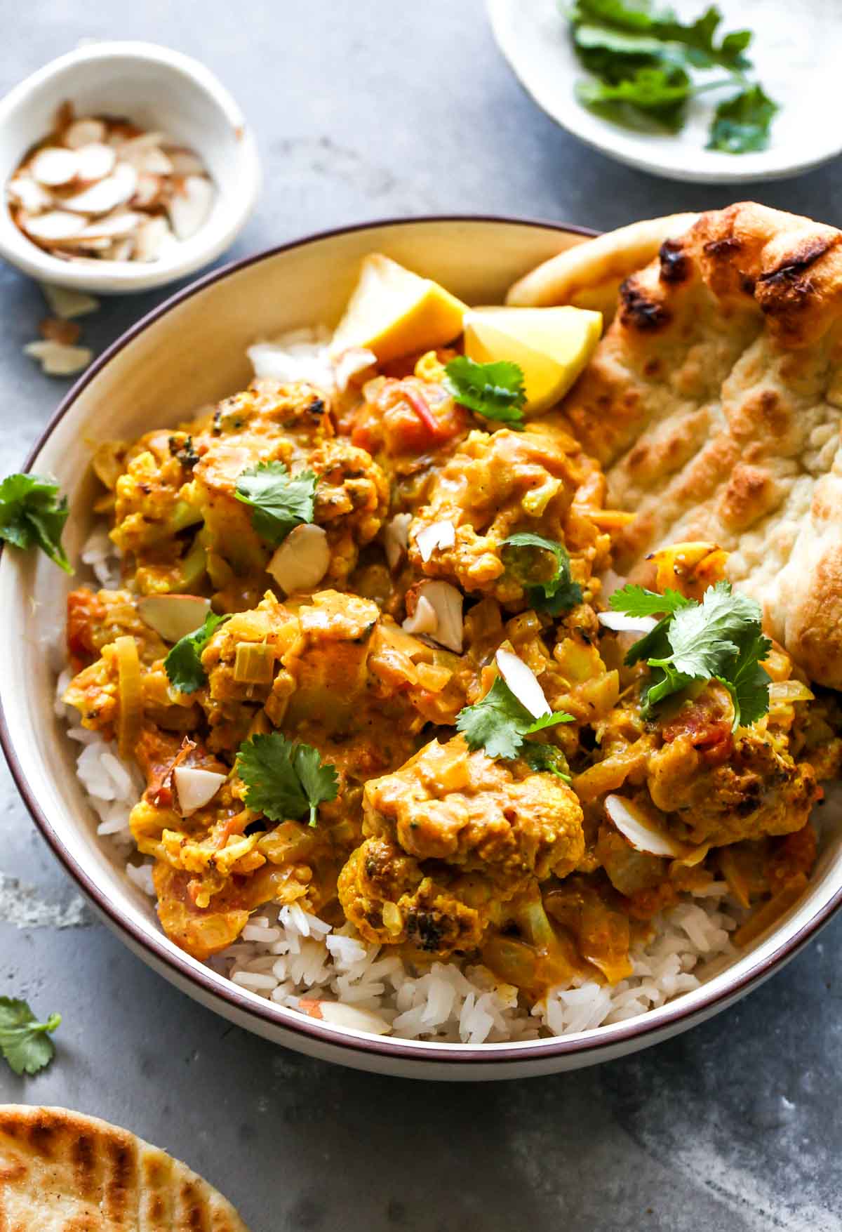 Cauliflower korma served in a tan bowl over rice with a side of naan bread