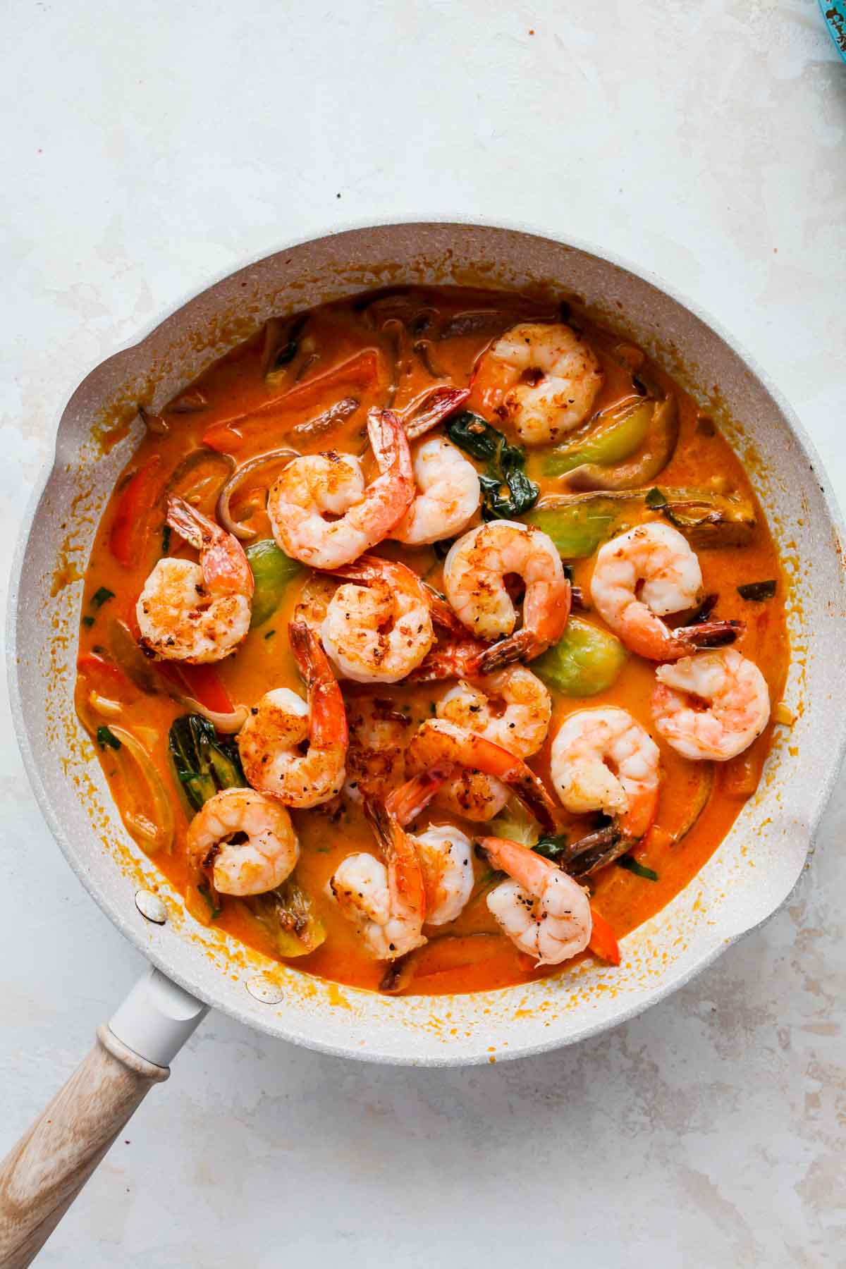Shrimp and basil being added to a skillet of veggies and curry sauce