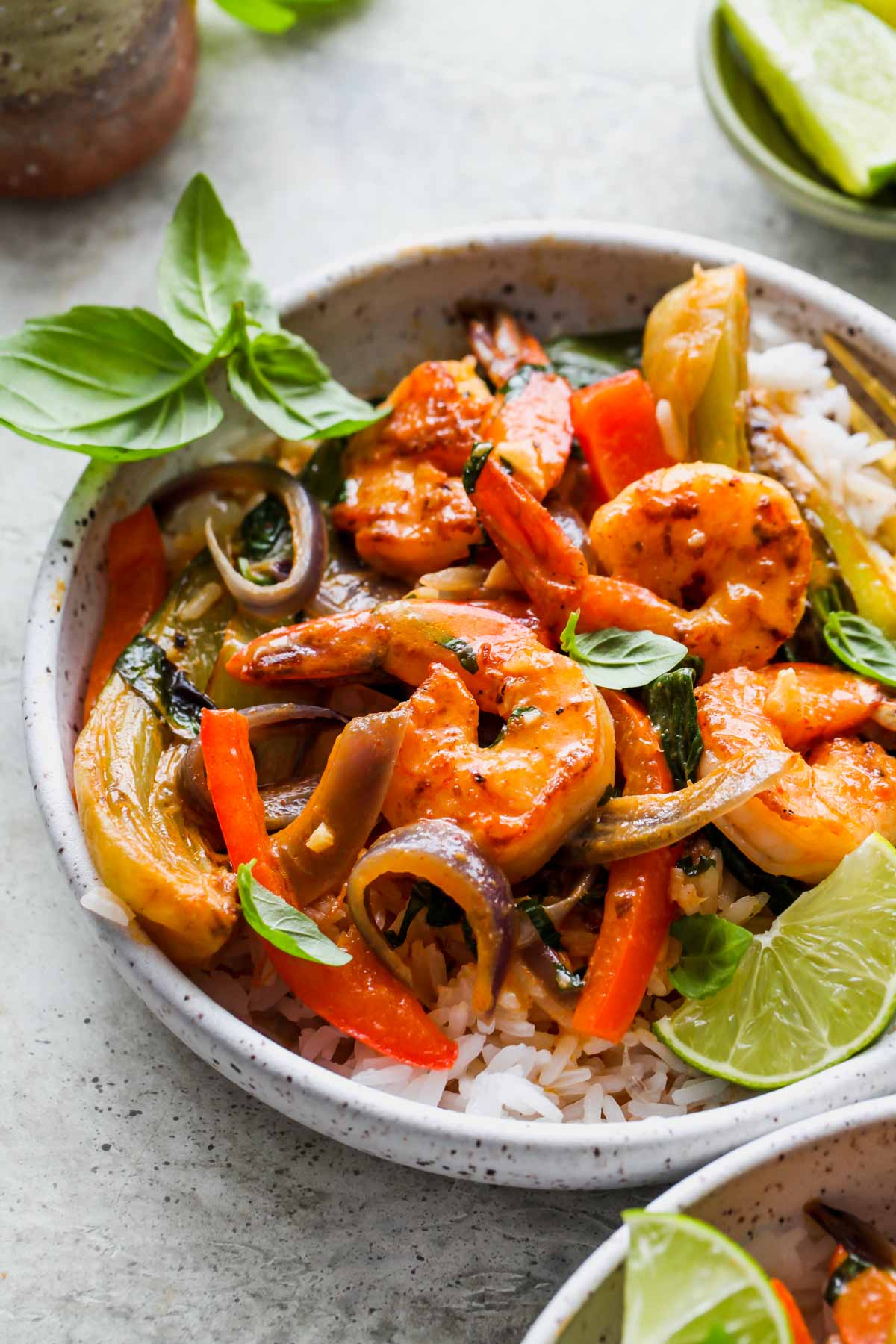 Red curry coconut shrimp and veggies in a white bowl topped with basil