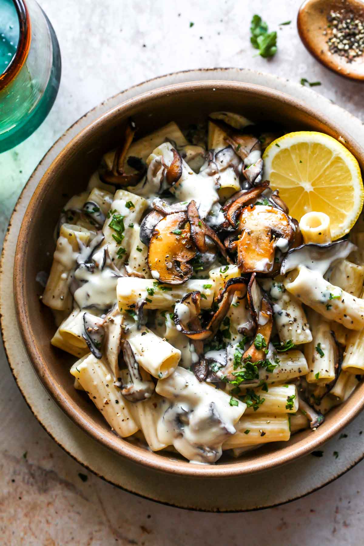 Rigatoni, mushrooms, and cashew-cream sauce in a gold bowl garnished with lemon
