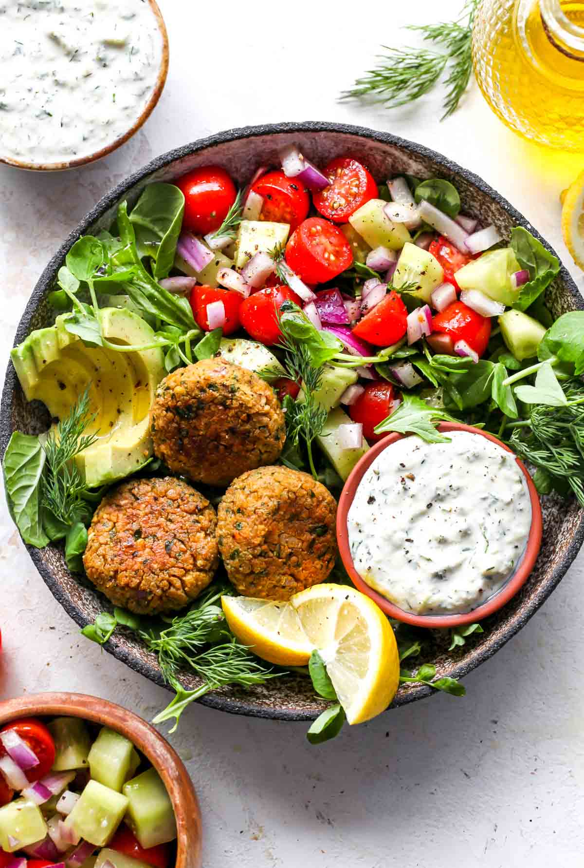 Chickpea falafel styled in a bowl with arugula, cashew tzatziki, and tomato-cucumber salad