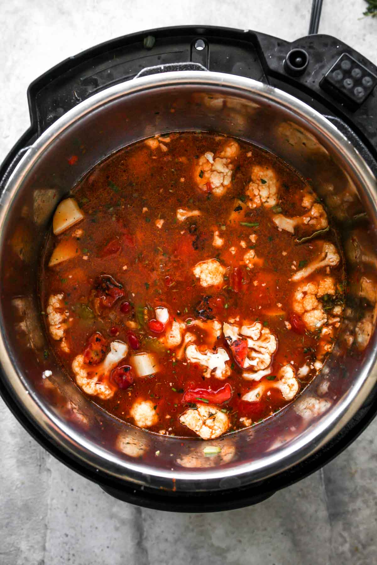 Tomatoes, broth, cauliflower, and potatoes being added to Instant Pot