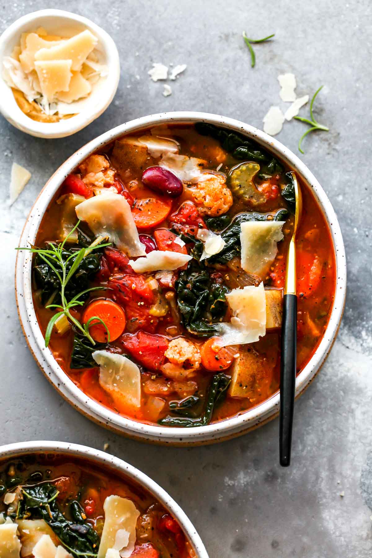 Vegetable soup in a white bowl topped with Parmesan and rosemary