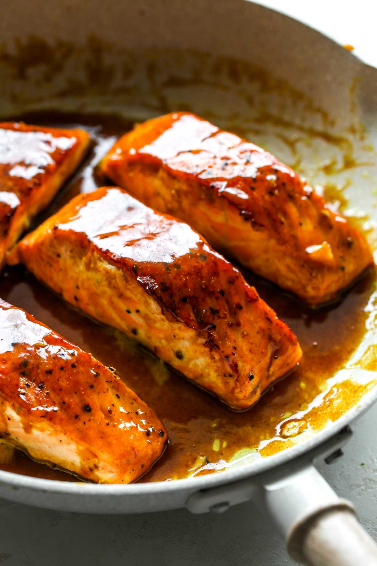 Four salmon fillets in a skillet coated in maple-mustard glaze