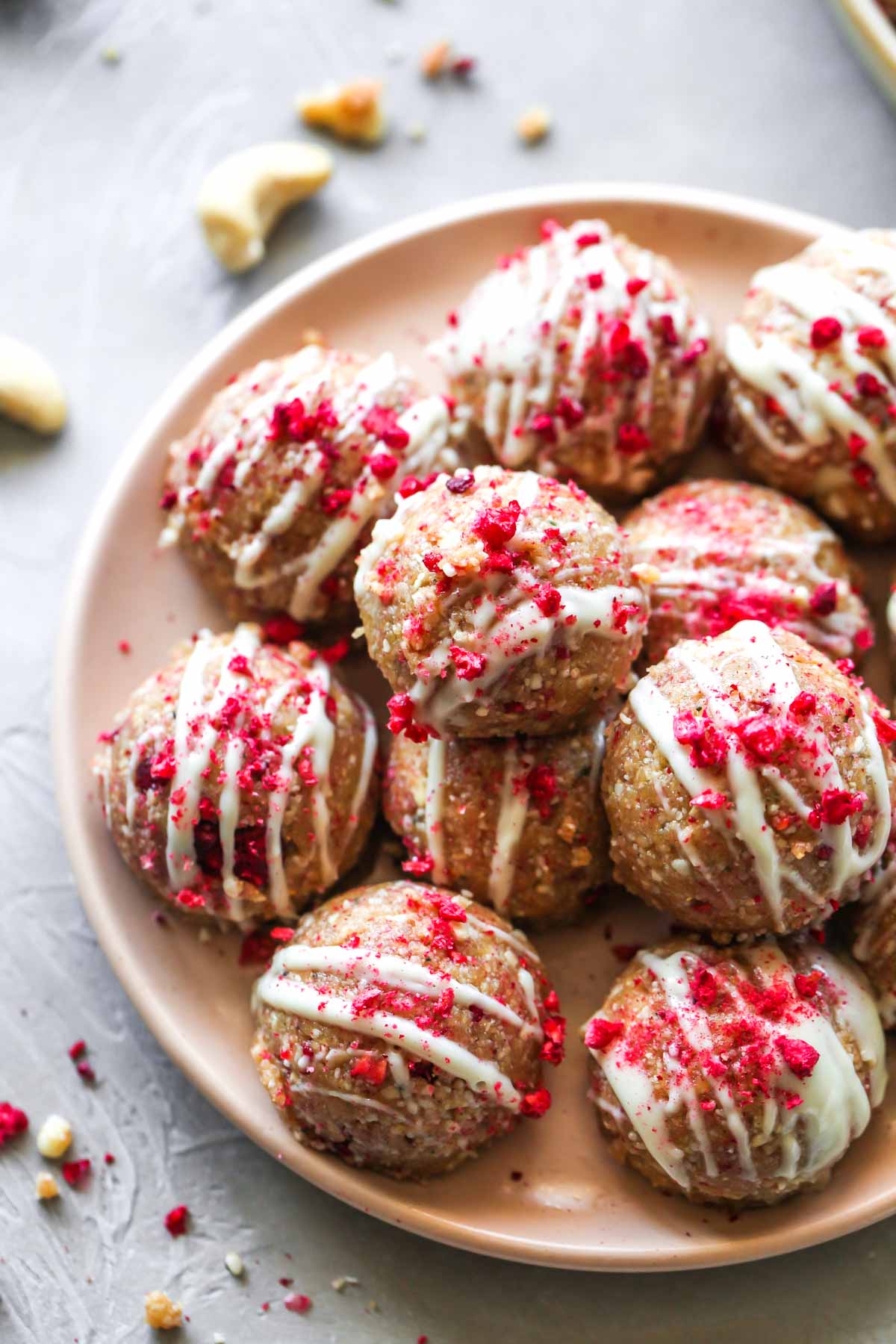 Energy bites with white chocolate drizzle and raspberries stacked on a plate