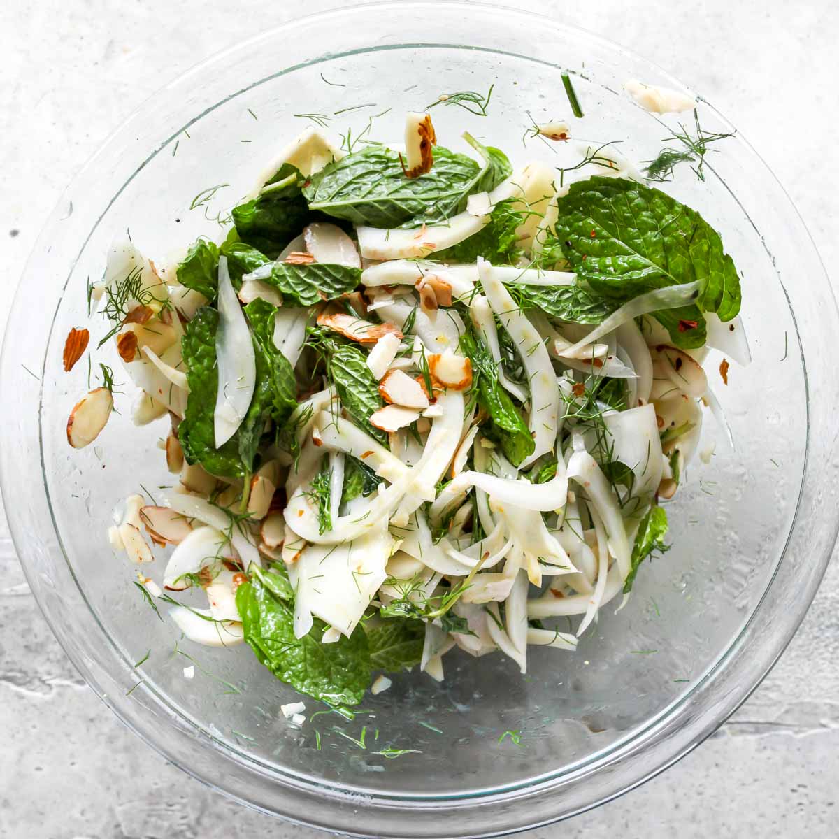 Shaved fennel, mint, and sliced almonds tossed in a clear bowl