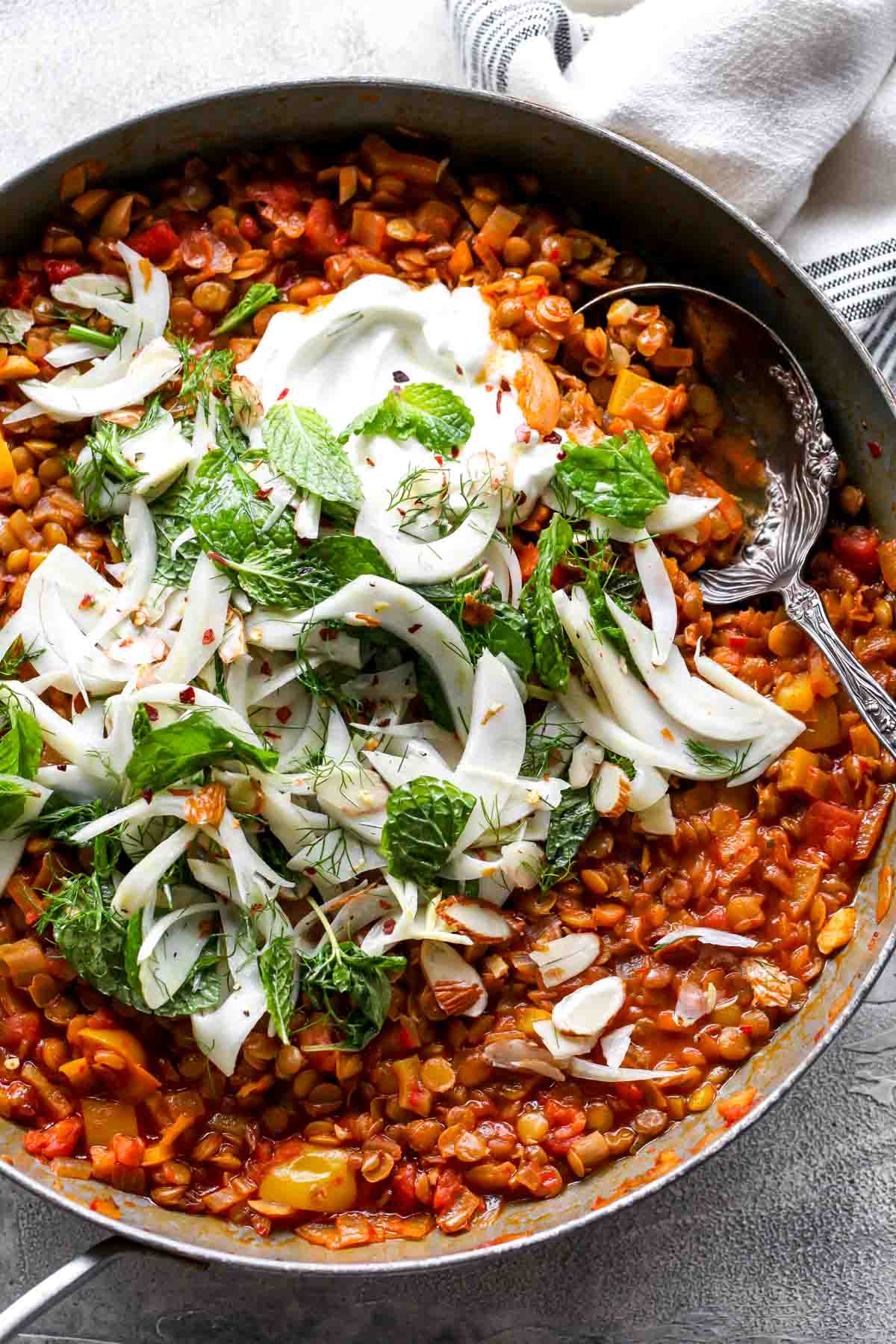 Stewed lentils in a skillet topped with shaved fennel salad