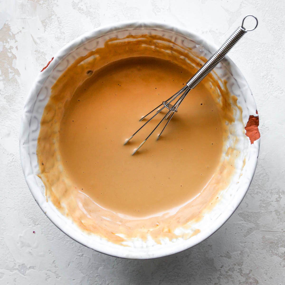 Tahini, adobo sauce, and lime juice being whisked together in a white bowl