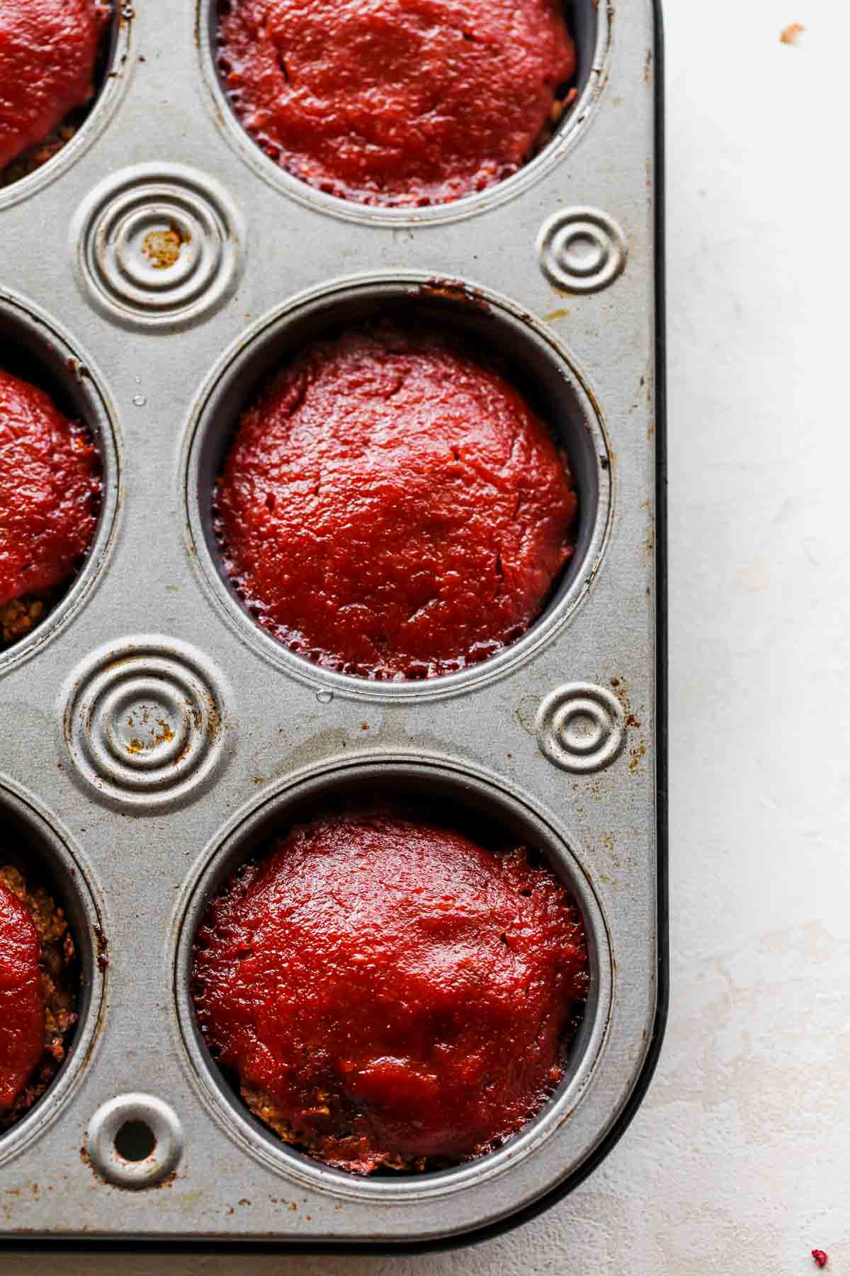 Mini meatloaves being topped with BBQ glaze and baked