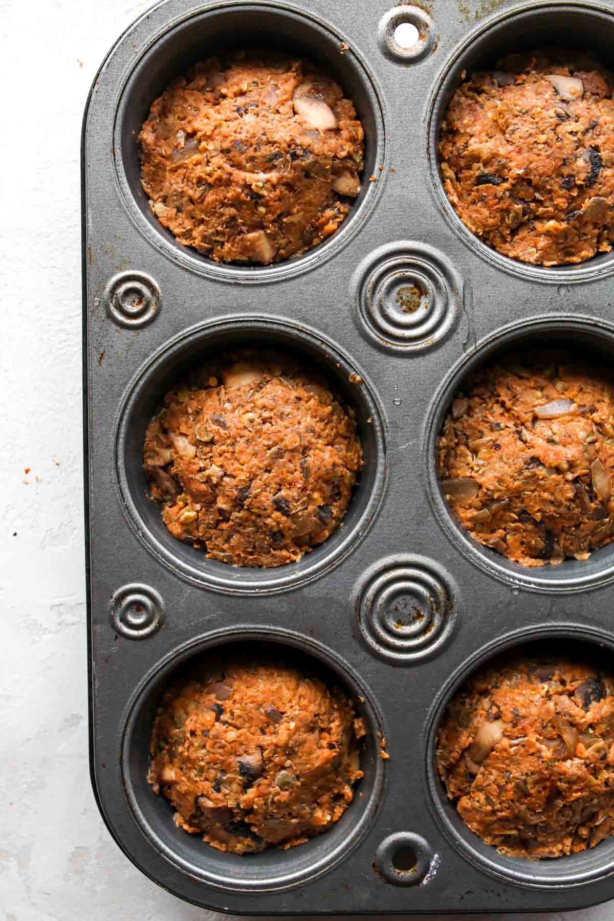 Vegetarian meatloaf mixture being pressed into muffin tins
