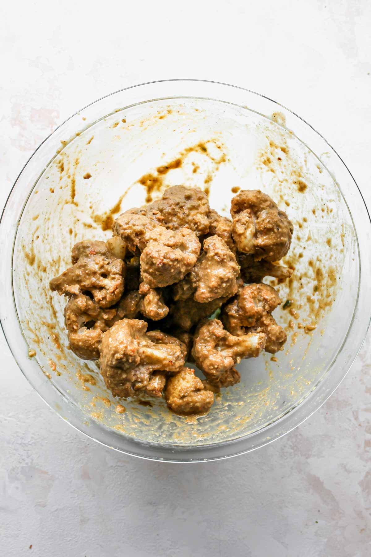 Baked cauliflower florets being tossed in jerk sauce in a large mixing bowl