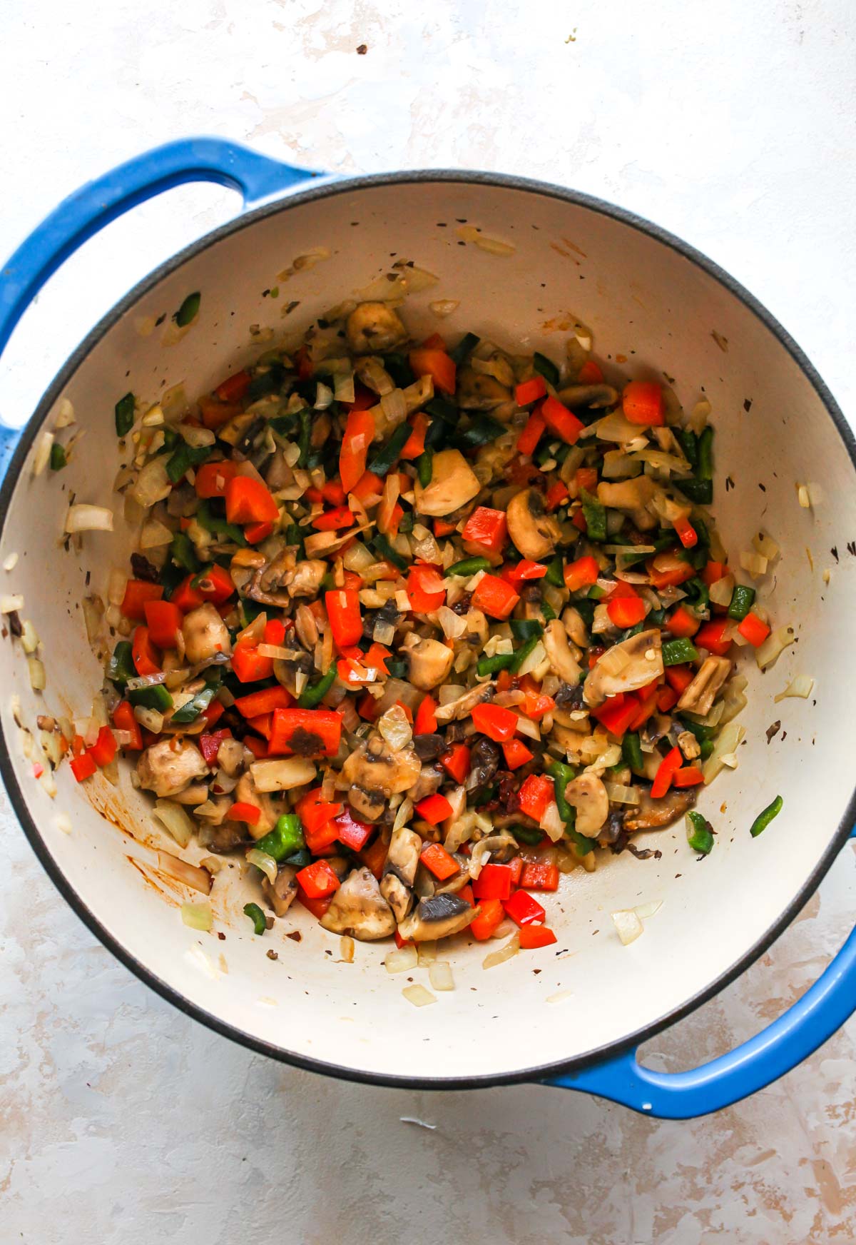 Mushrooms, peppers, and onions being sauteed in a Dutch oven