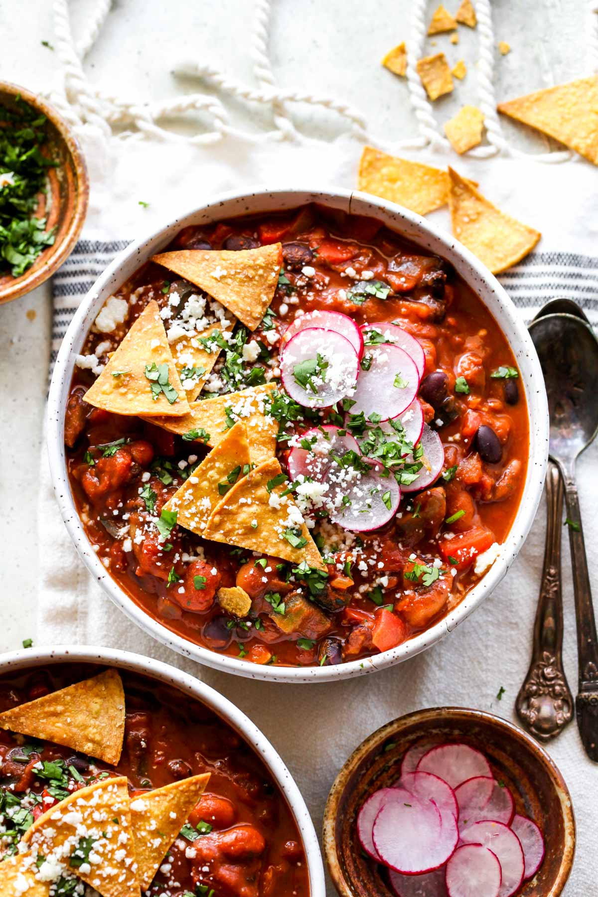 Vegetarian chili in a white bowl topped with radish, cilantro, and chips
