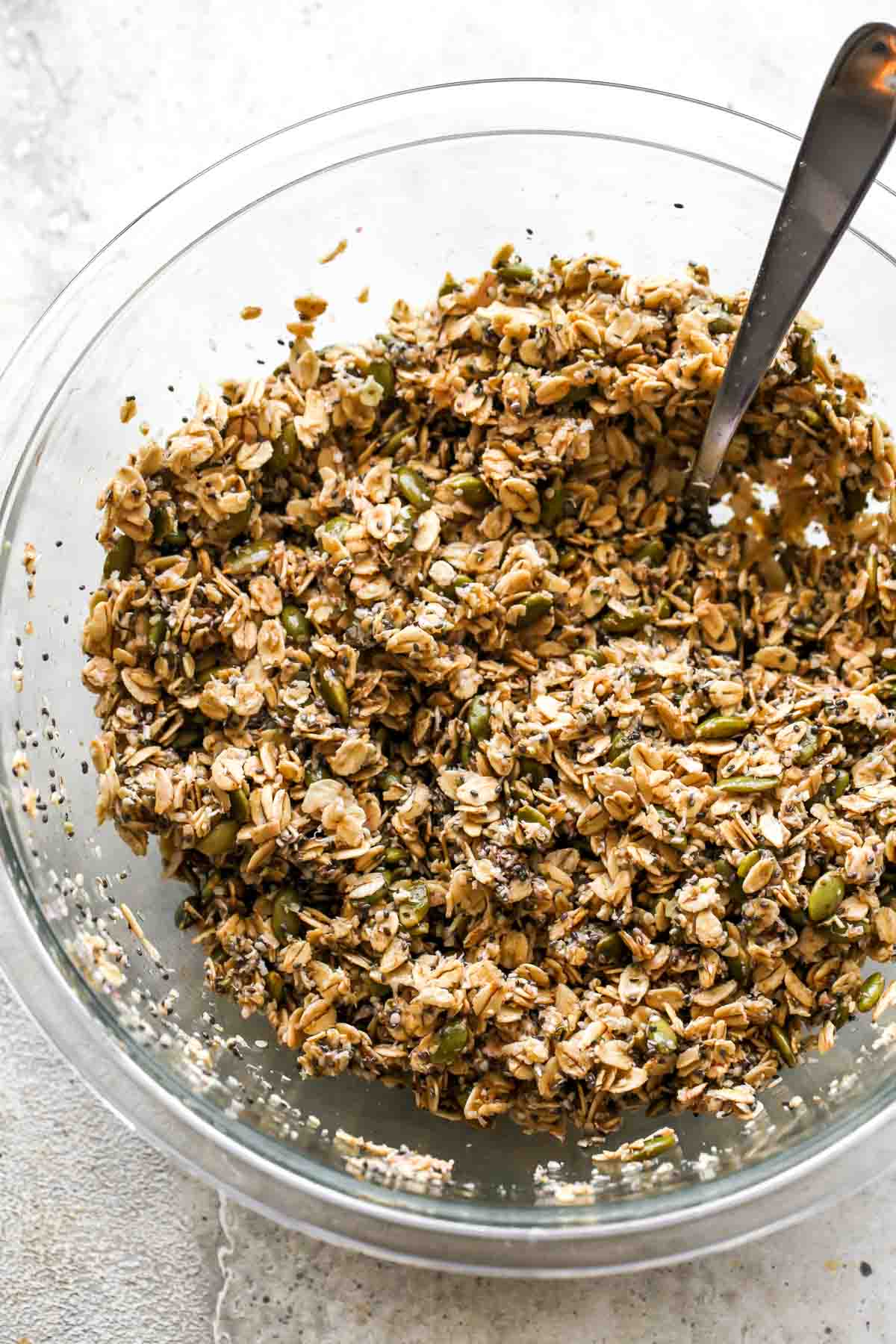 Oats, seeds, coconut, oil, and honey being mixed together with a spoon