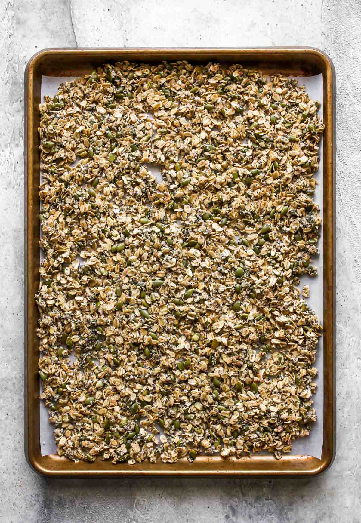 Raw granola being spread on a rimmed baking sheet and baked until golden