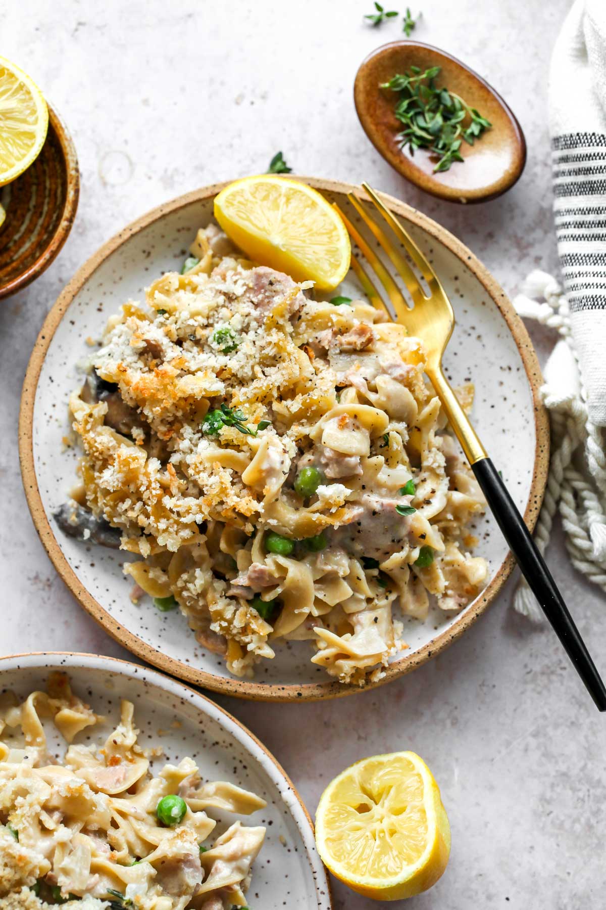 Tuna casserole being plated and served with lemon wedges and fresh thyme