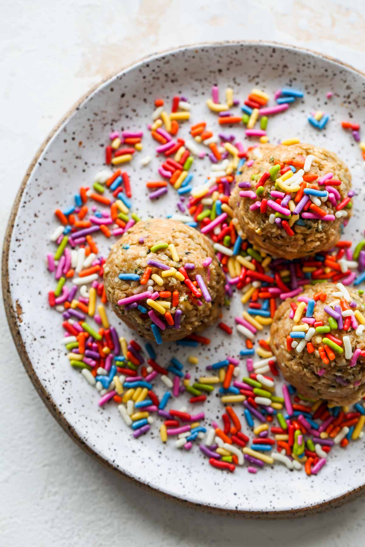 Protein balls being rolled in sprinkles on a white plate
