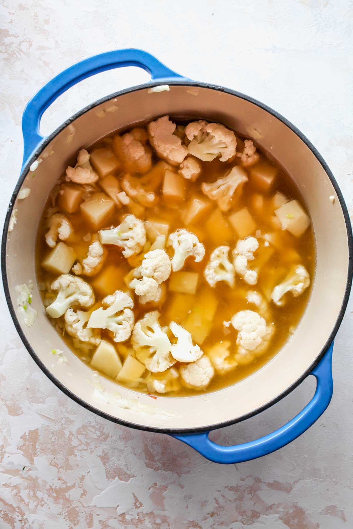 Broth being poured into a Dutch oven of soup