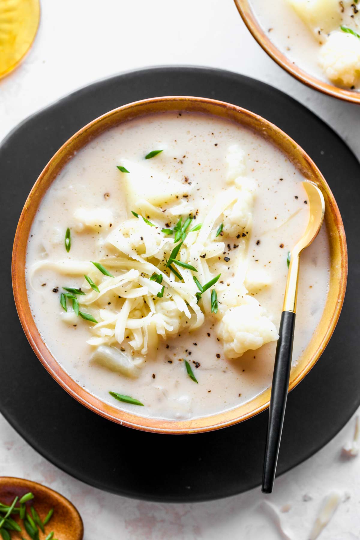 Cheesy cauliflower soup in a gold bowl on a black plate