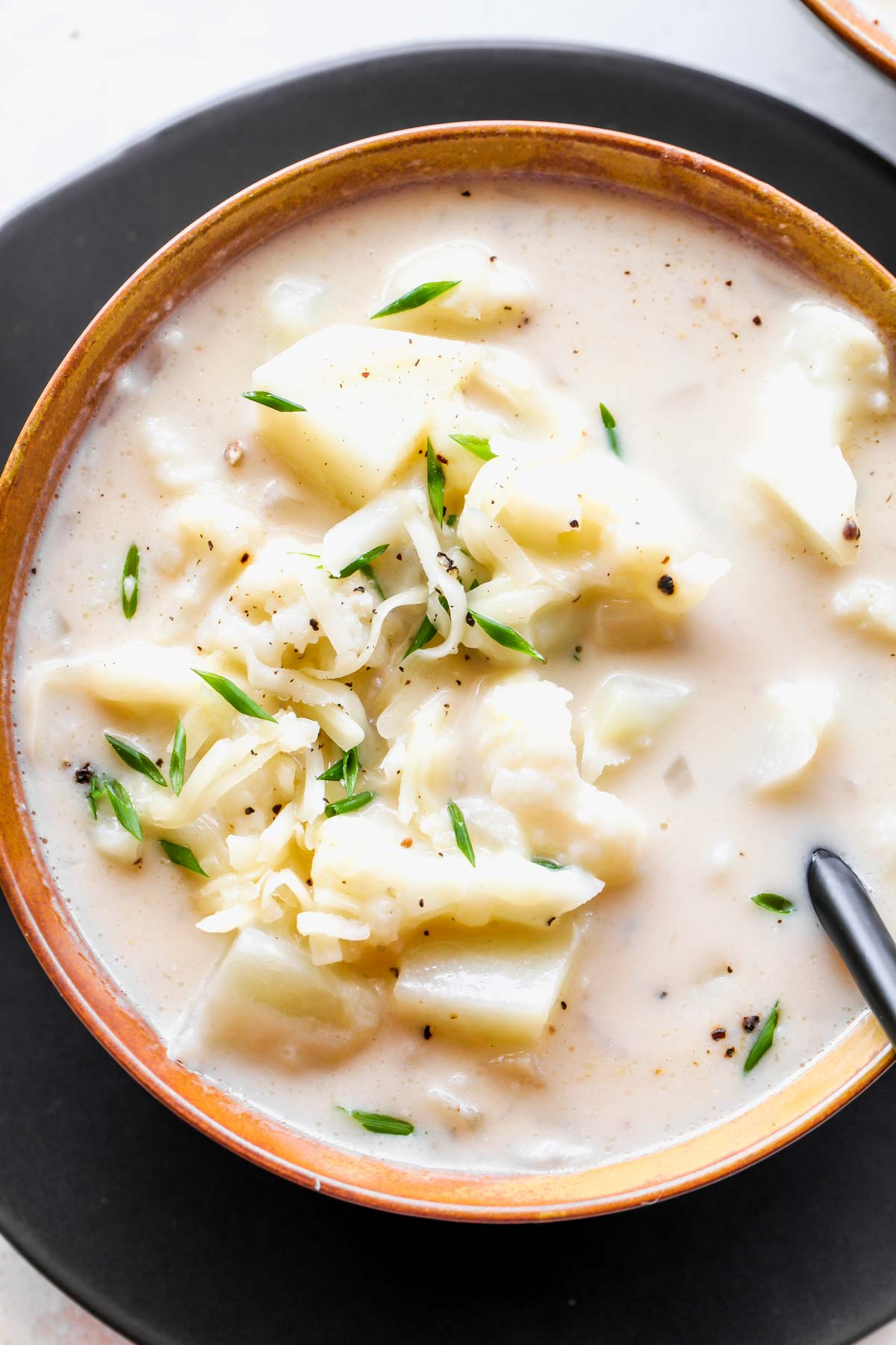 Spoon digging into a bowl of cheesy cauliflower soup