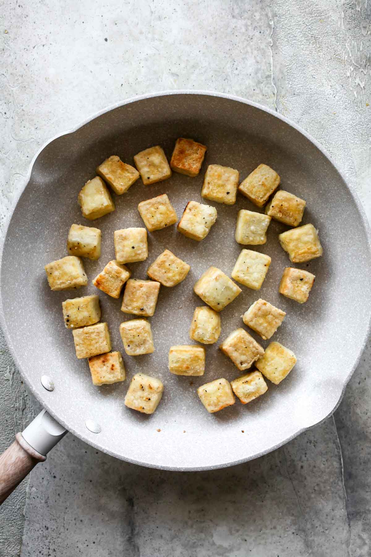 Tofu cubes sauteing in a white skillet