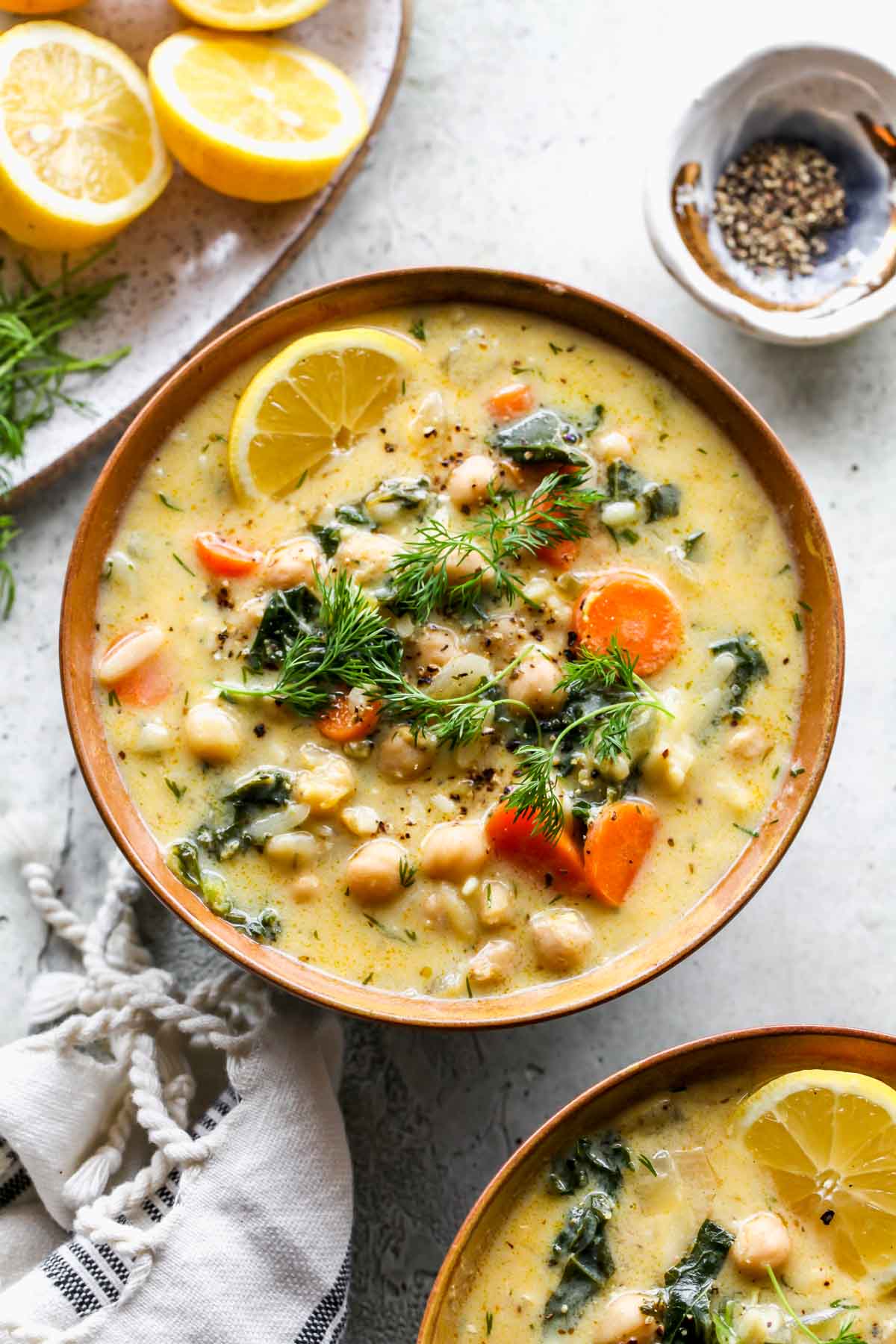 Chickpea and vegetable soup in a gold bowl topped with fresh dill and lemon