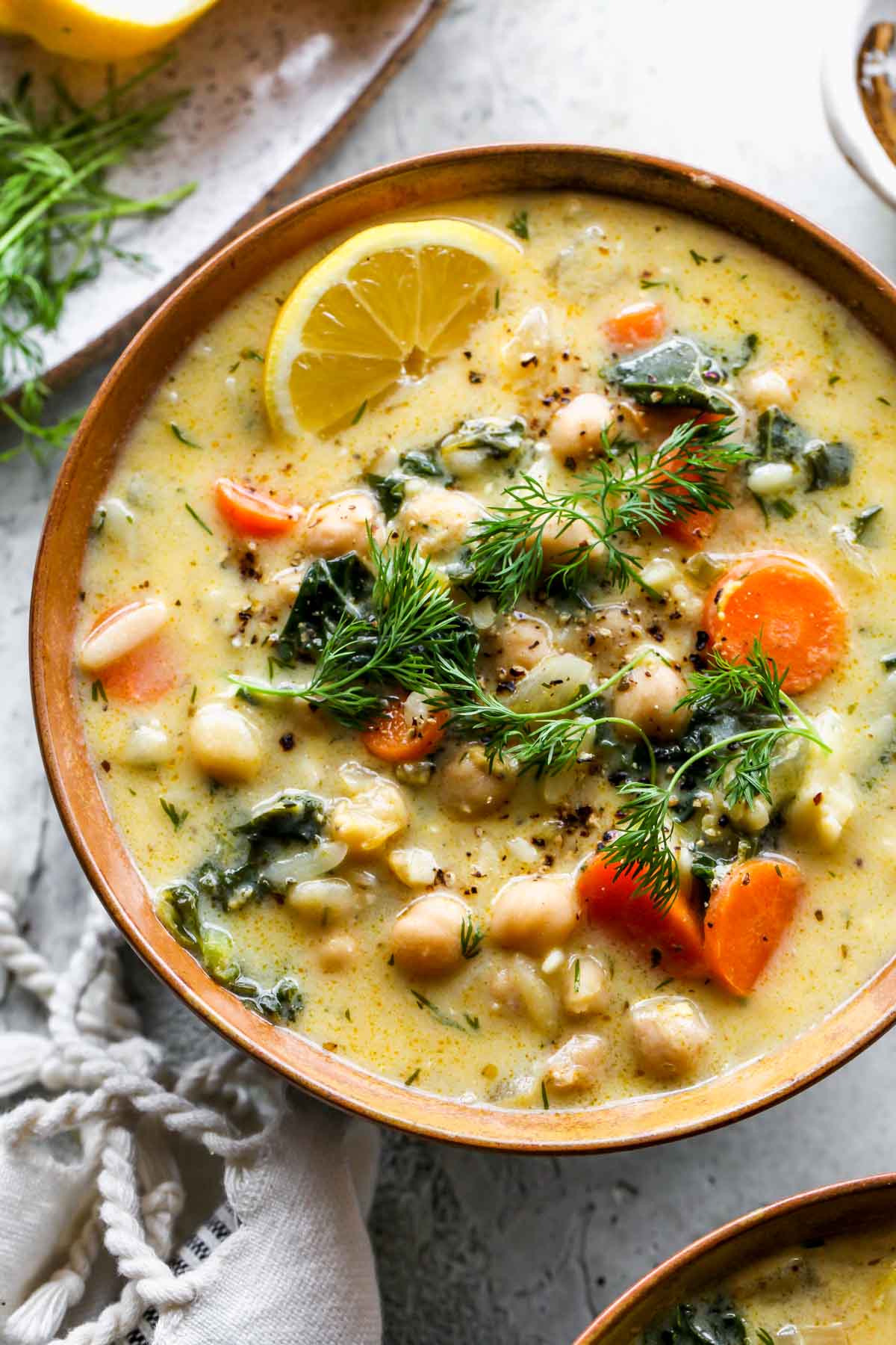 Single serving of greek chickpea soup in a gold bowl topped with fresh herbs