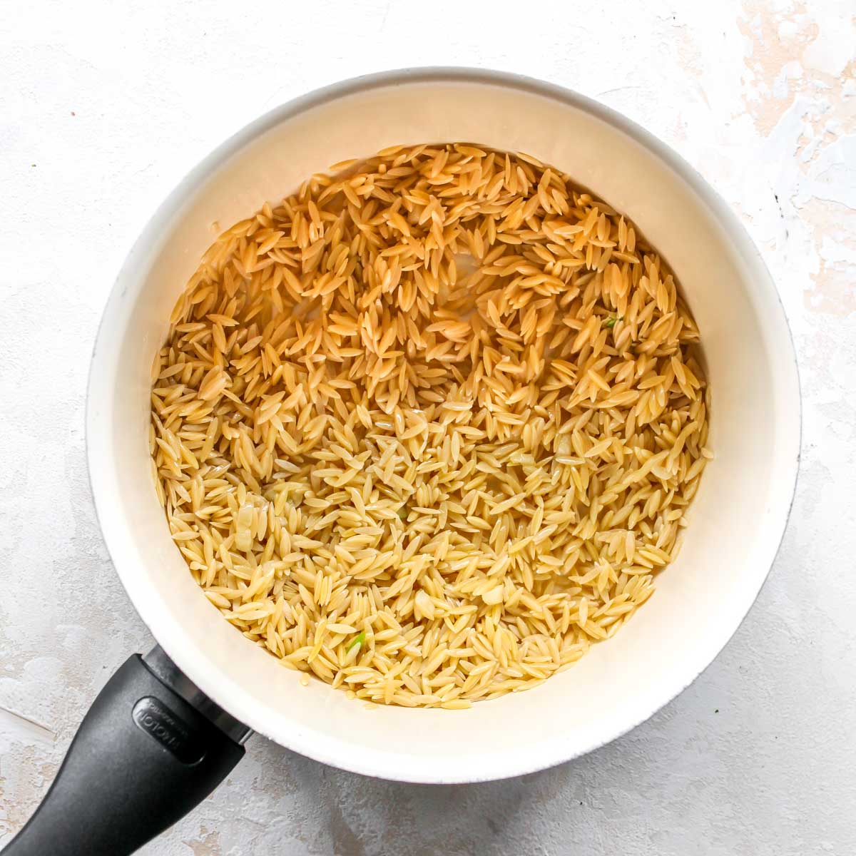 Pasta grains being toasted in butter in a saucepan