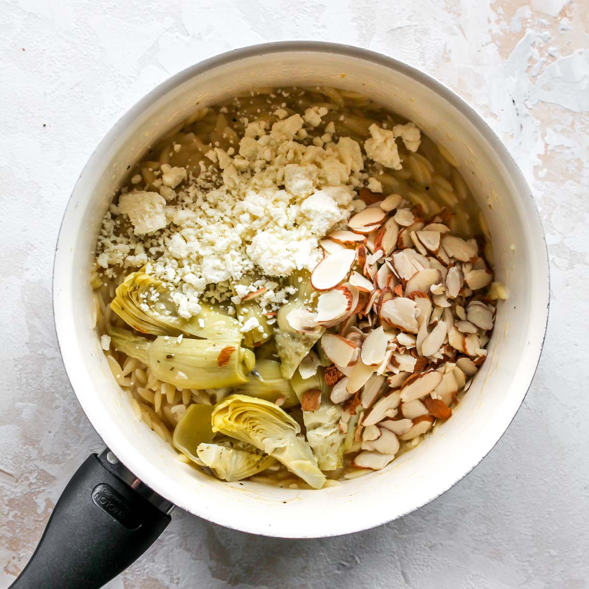Artichokes, almonds, and feta being mixed in a saucepan
