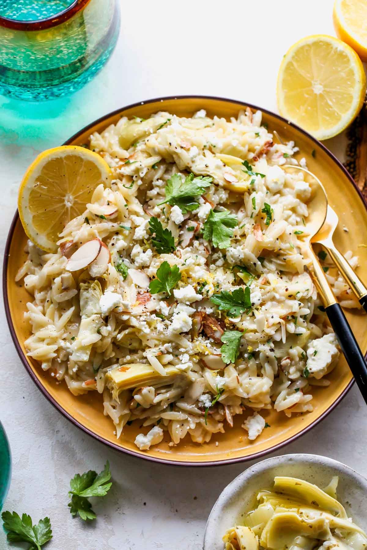 Lemon Artichoke Orzo Salad styled on a yellow plate with lemon wedges